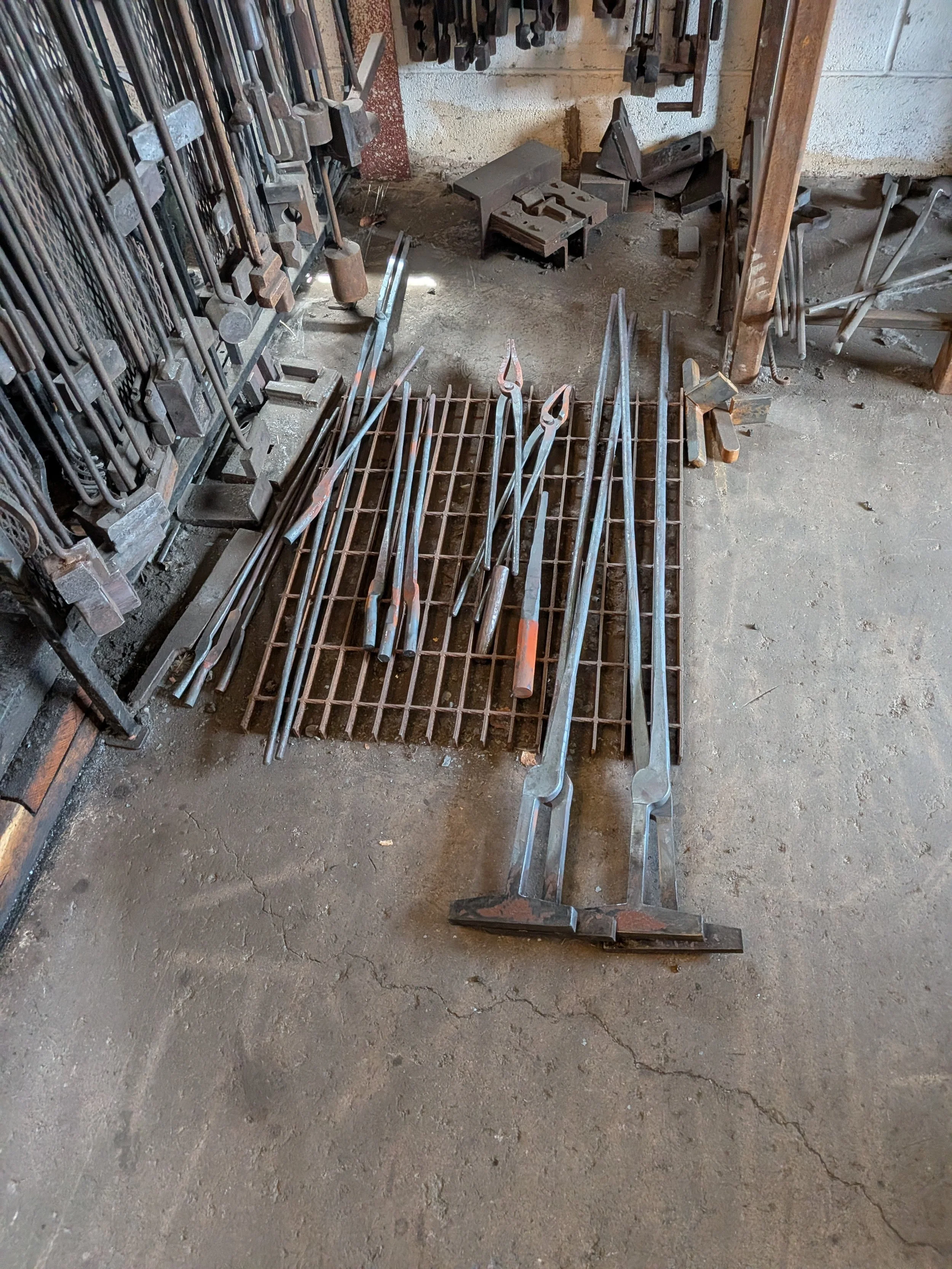 Blacksmithing tongs in various levels of completion on the floor.
