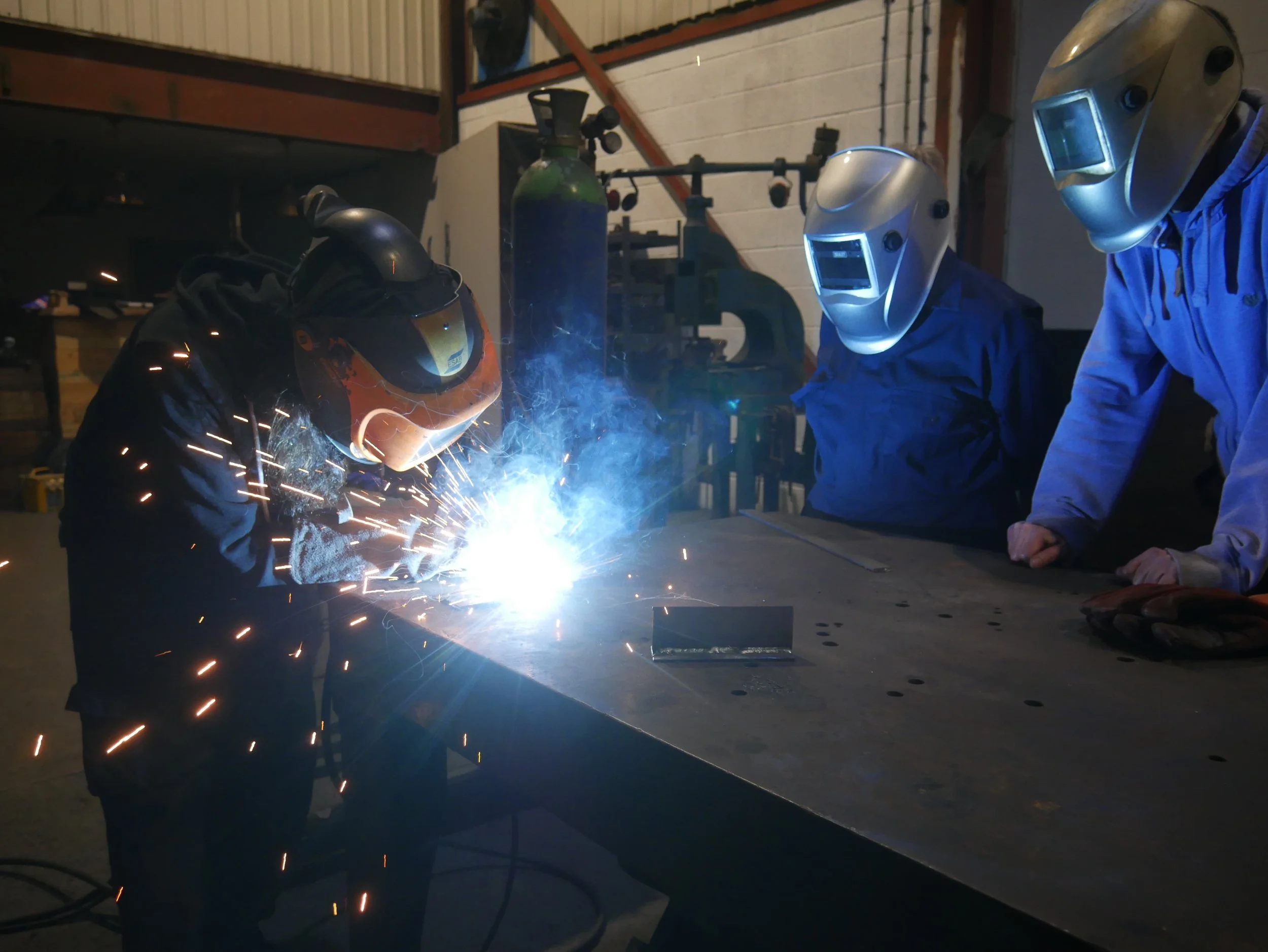 Welding instructor demonstrating a weld in front of a couple of students with welding masks on