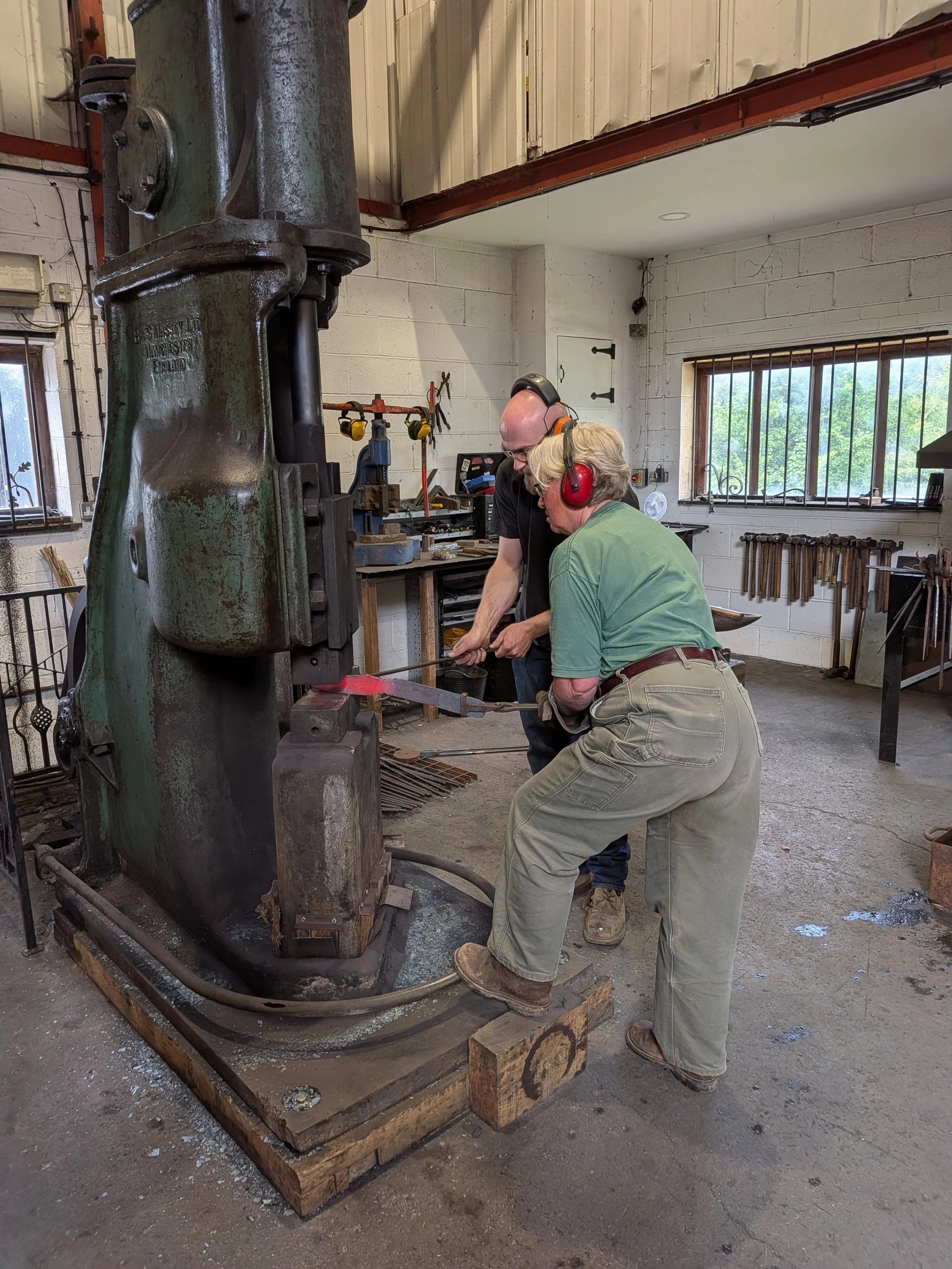 A blacksmith teaching a student how to work on a Damascus billet with a powerhammer