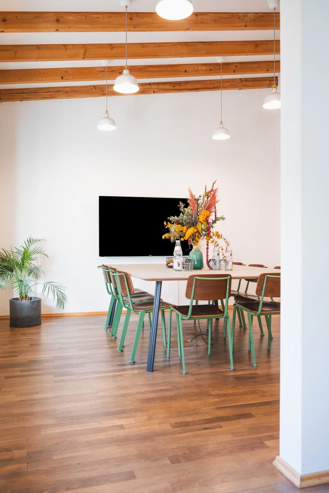 Heller und moderner Besprechungsraum der Neuen Remise mit Holzbalkendecke, einem langen Tisch und bequemen Stühlen. Der Raum ist mit einem großen Bildschirm und frischen Blumen dekoriert, ideal für produktive Meetings und Strategietreffen