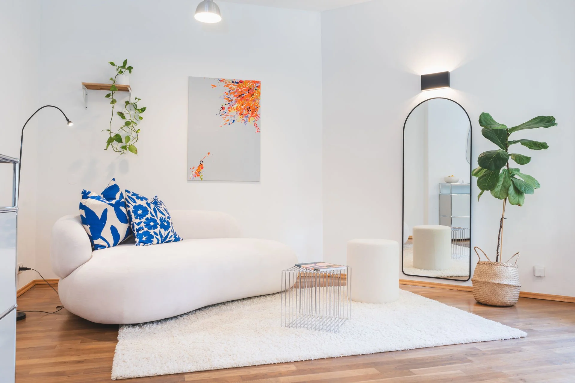 Gemütlicher Besprechungsraum der Neuen Remise mit modernen Möbeln, einem weißen Sofa, bunten Kissen und einem eleganten Spiegel. Der Raum bietet eine inspirierende Atmosphäre mit natürlichen Pflanzen und einem klaren, minimalistischen Design.