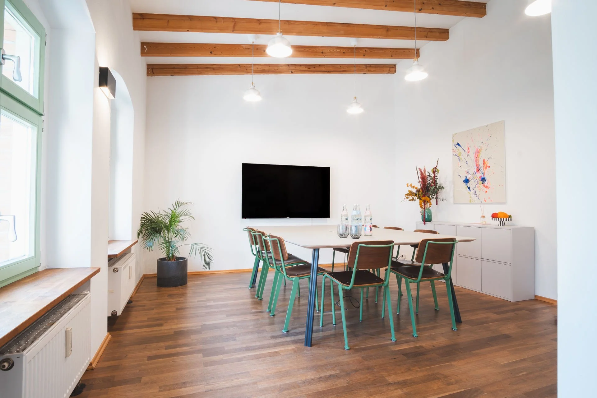 Moderner Besprechungsraum der Neuen Remise mit Holzbalkendecke, einem eleganten Tisch und bequemen Stühlen. Der Raum ist mit einer großen Wandtafel und frischen Blumen dekoriert, ideal für produktive Meetings und kreative Workshops.