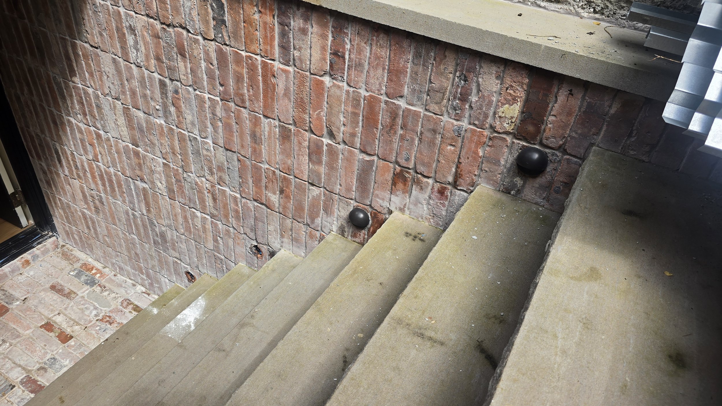 Concrete stairs next to a brick wall with black hemispherical lighting on the wall near the stairs.
