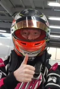 Un pilote de course en tenue de pilotage avec casque, faisant un signe de la main.