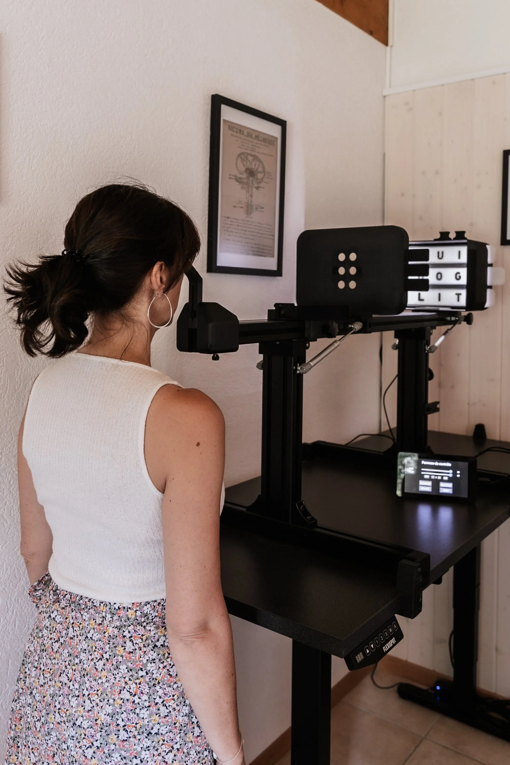 Une femme regarde un appareil d'orthophonie avec des lettres lumineuses sur un support en noir.