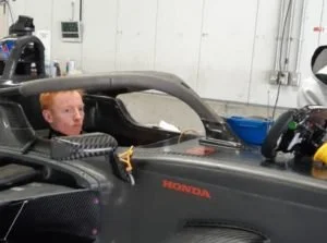 Un enfant assis dans un simulateur de course de voiture Honda, à l'intérieur d'une pièce ou d'un garage