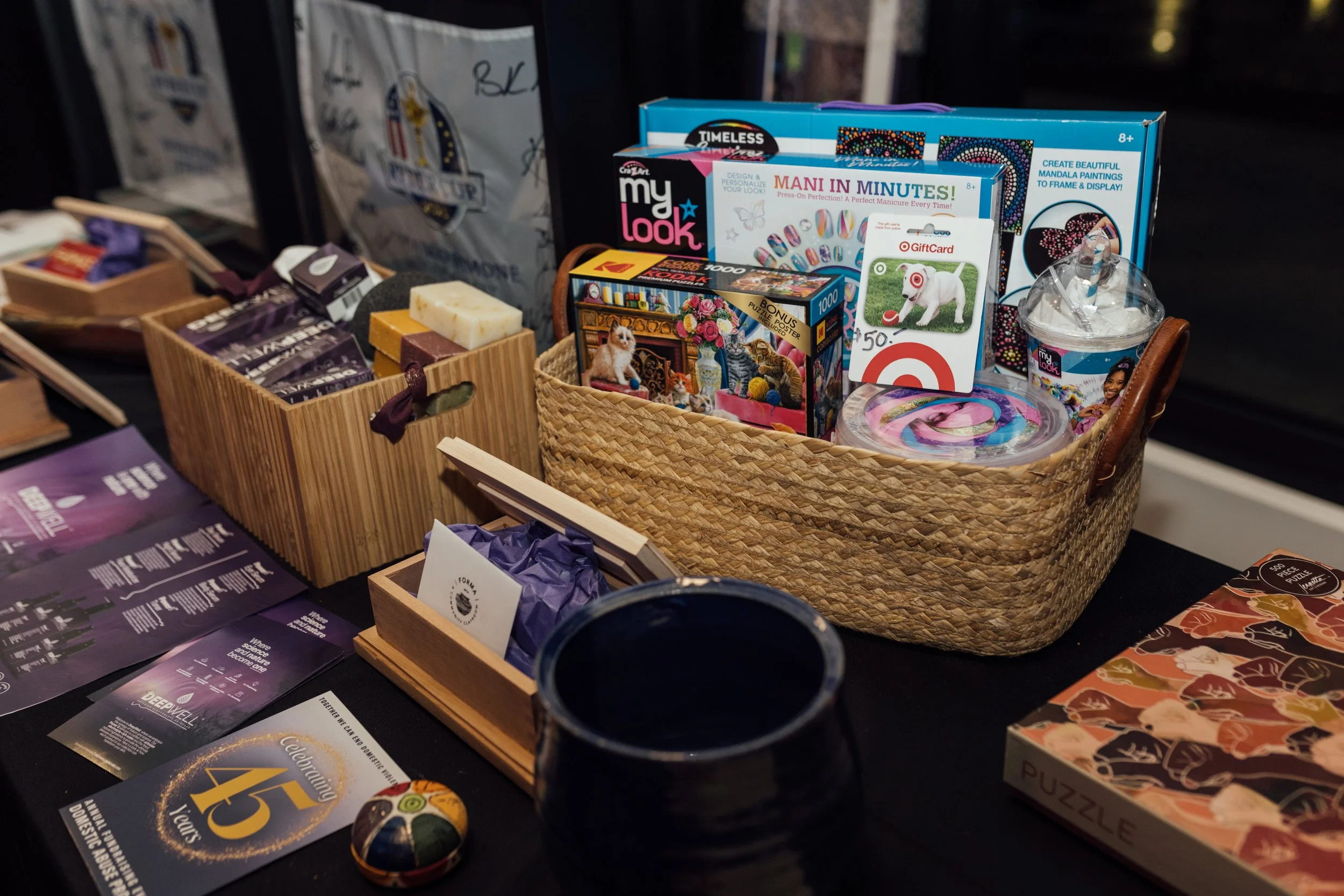 A display of various gift items and accessories arranged in woven baskets on a table, including beauty and wellness products, children's toys, and puzzles.