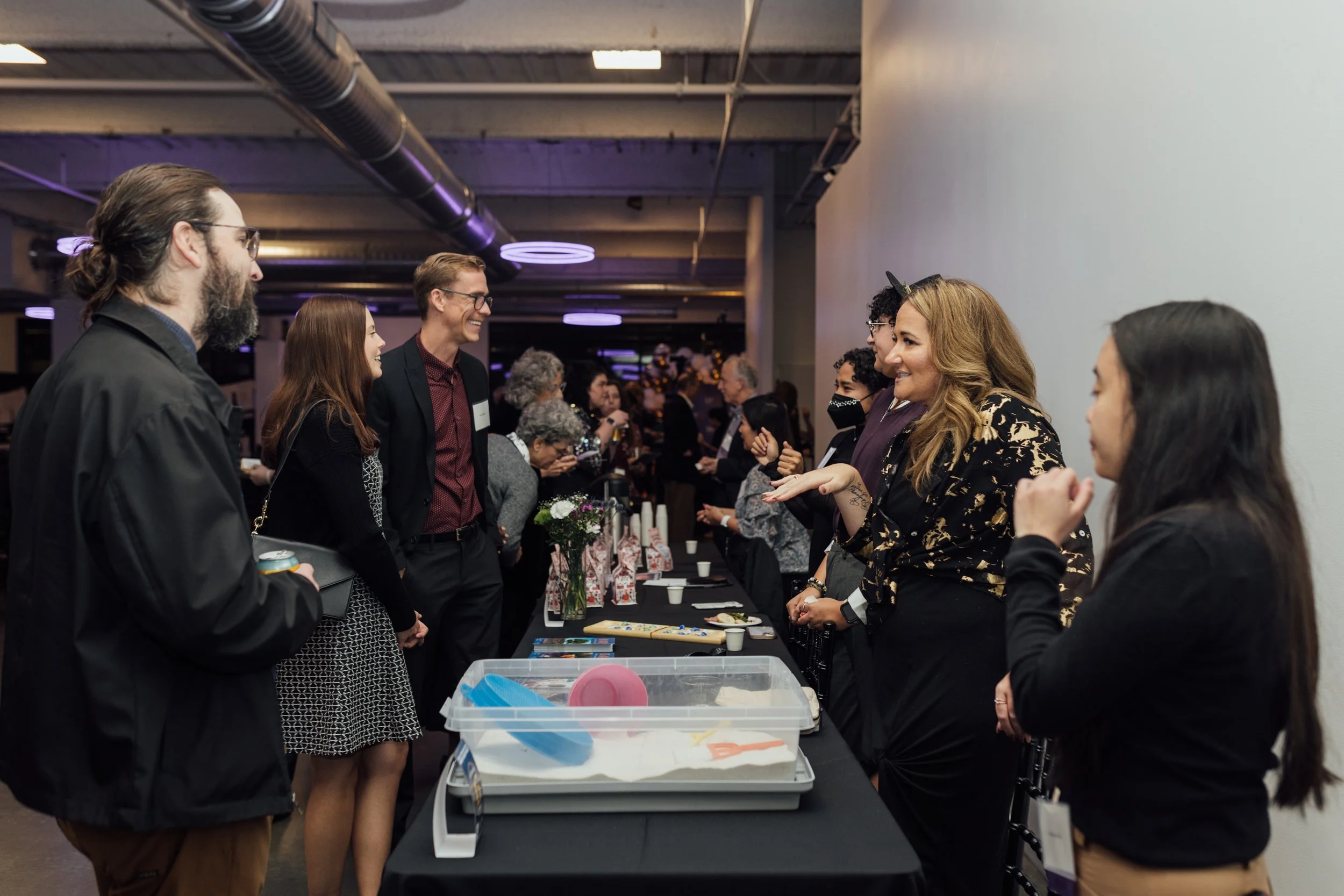 People socializing at a networking event with a table of name tags and informational materials.