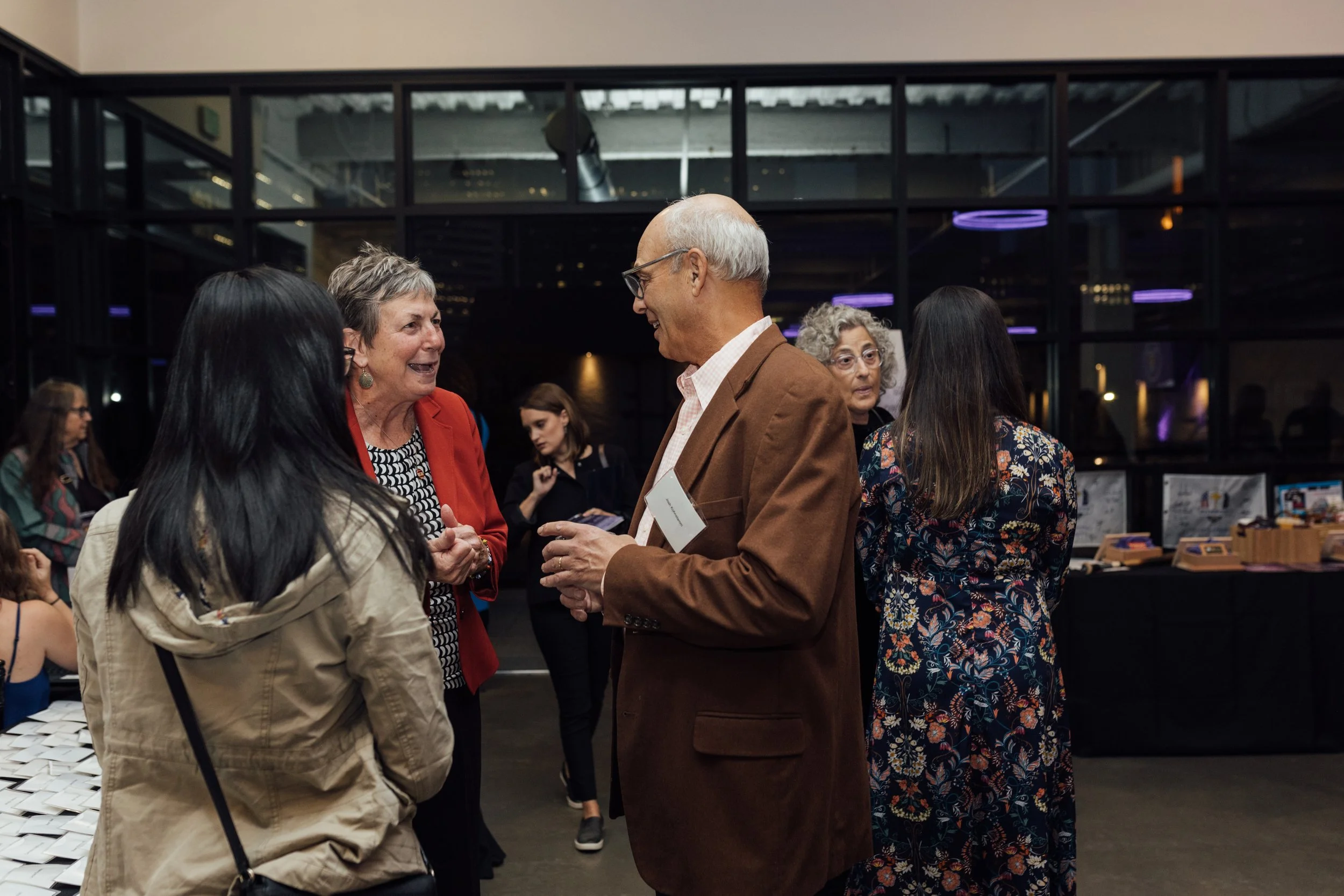 Group of people at a social event, engaging in conversation indoors near a table with items on display.