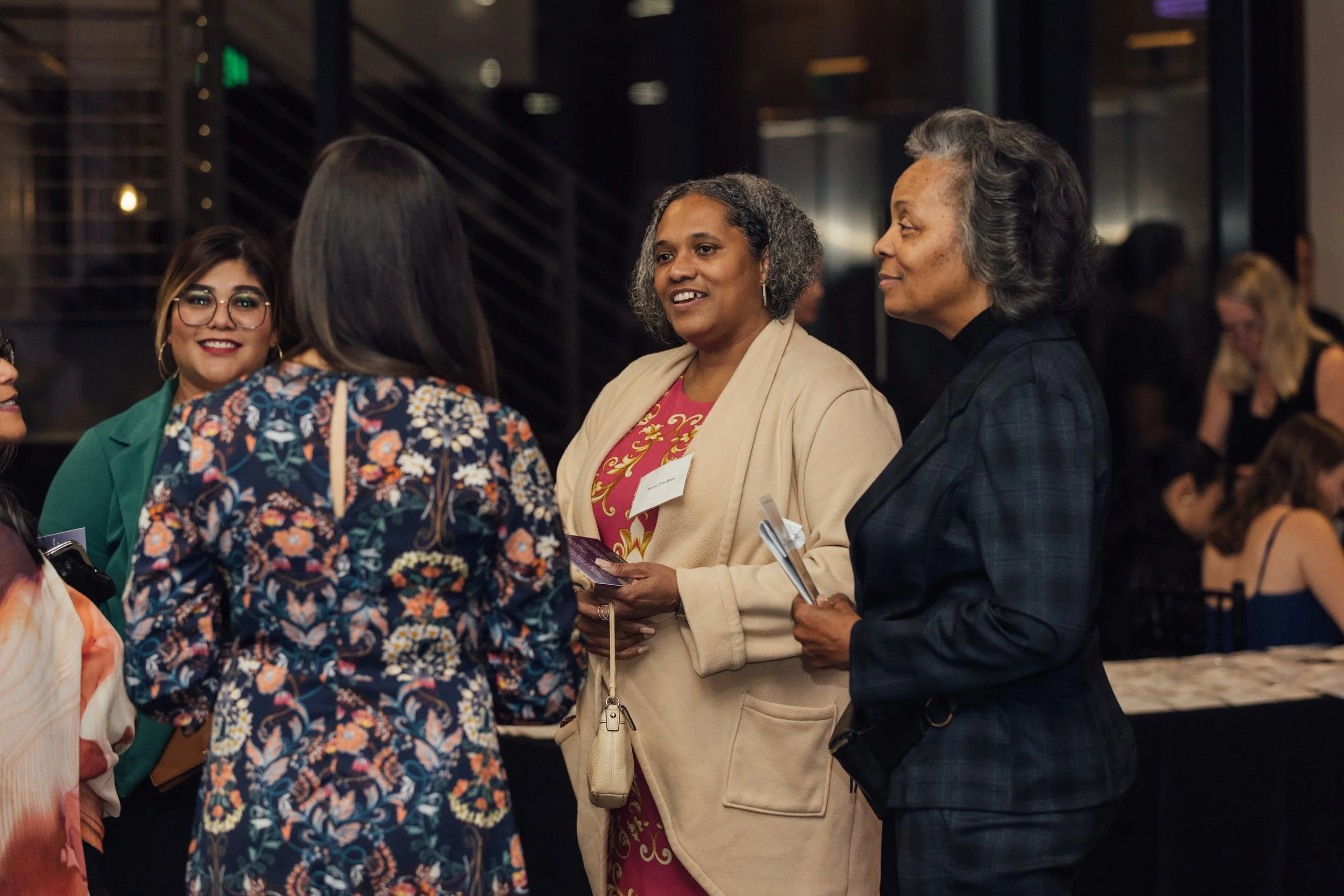 Group of women engaged in conversation at a social event in a modern indoor space.