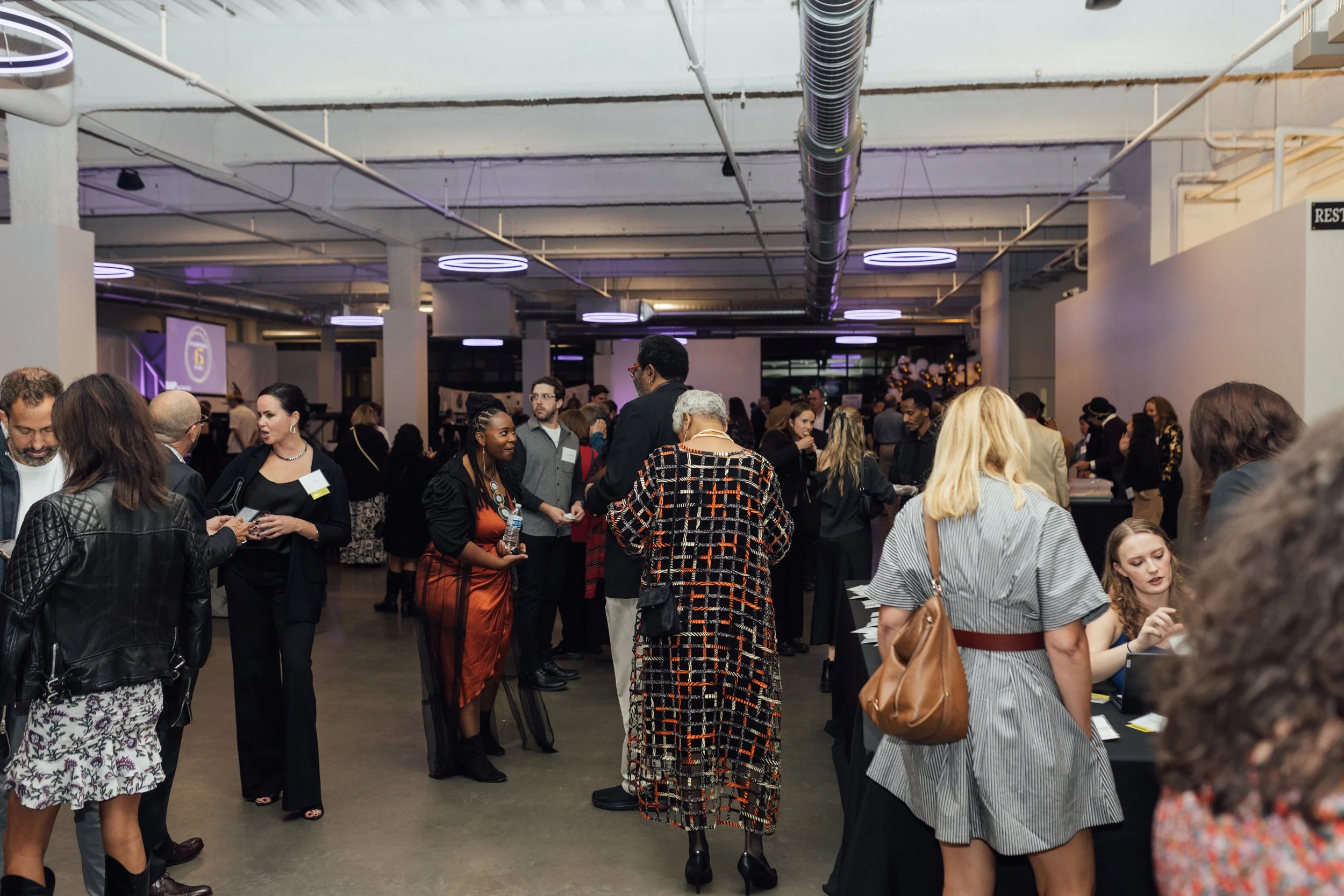 People attending a networking event or social gathering in a modern indoor space with purple lighting and industrial decor.