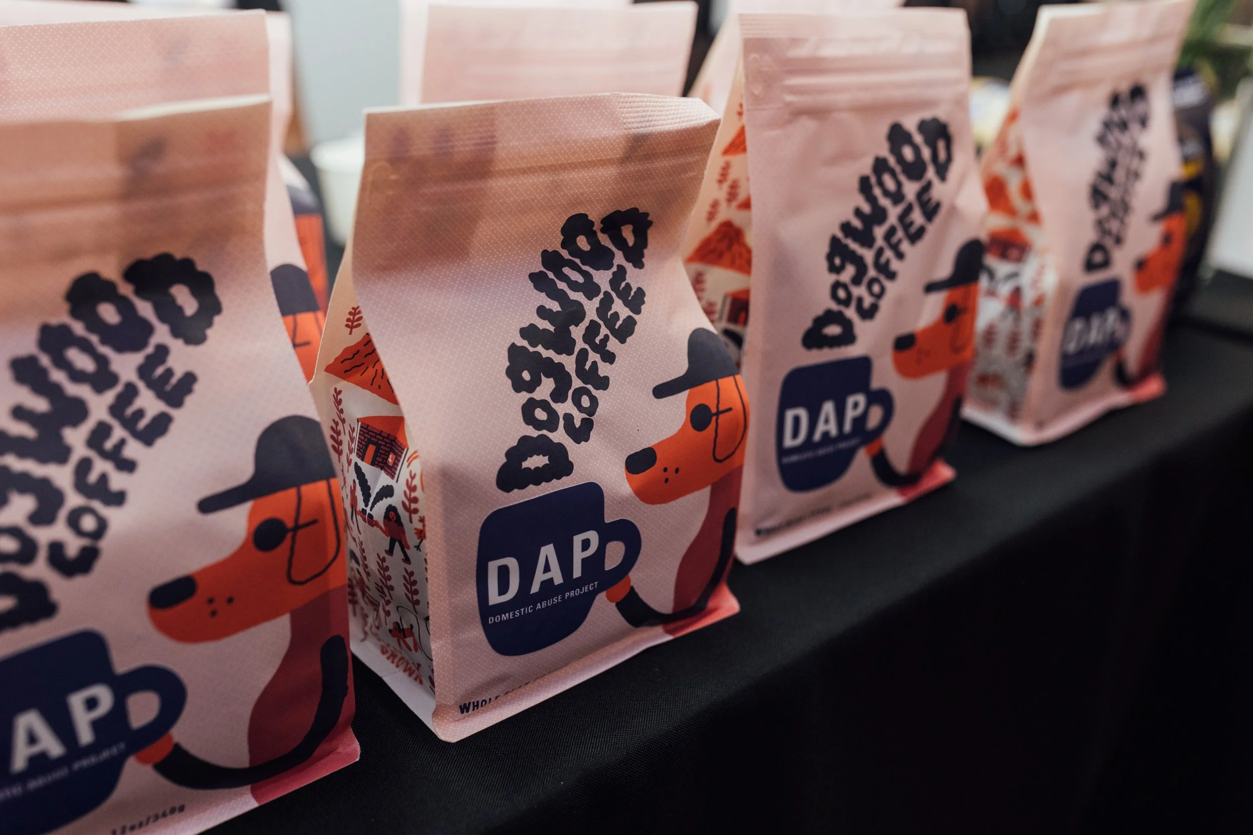 Pink bags labeled 'Dog Coffee' with an illustration of a dog wearing a hat and the logo 'DAD' arranged on a black surface.