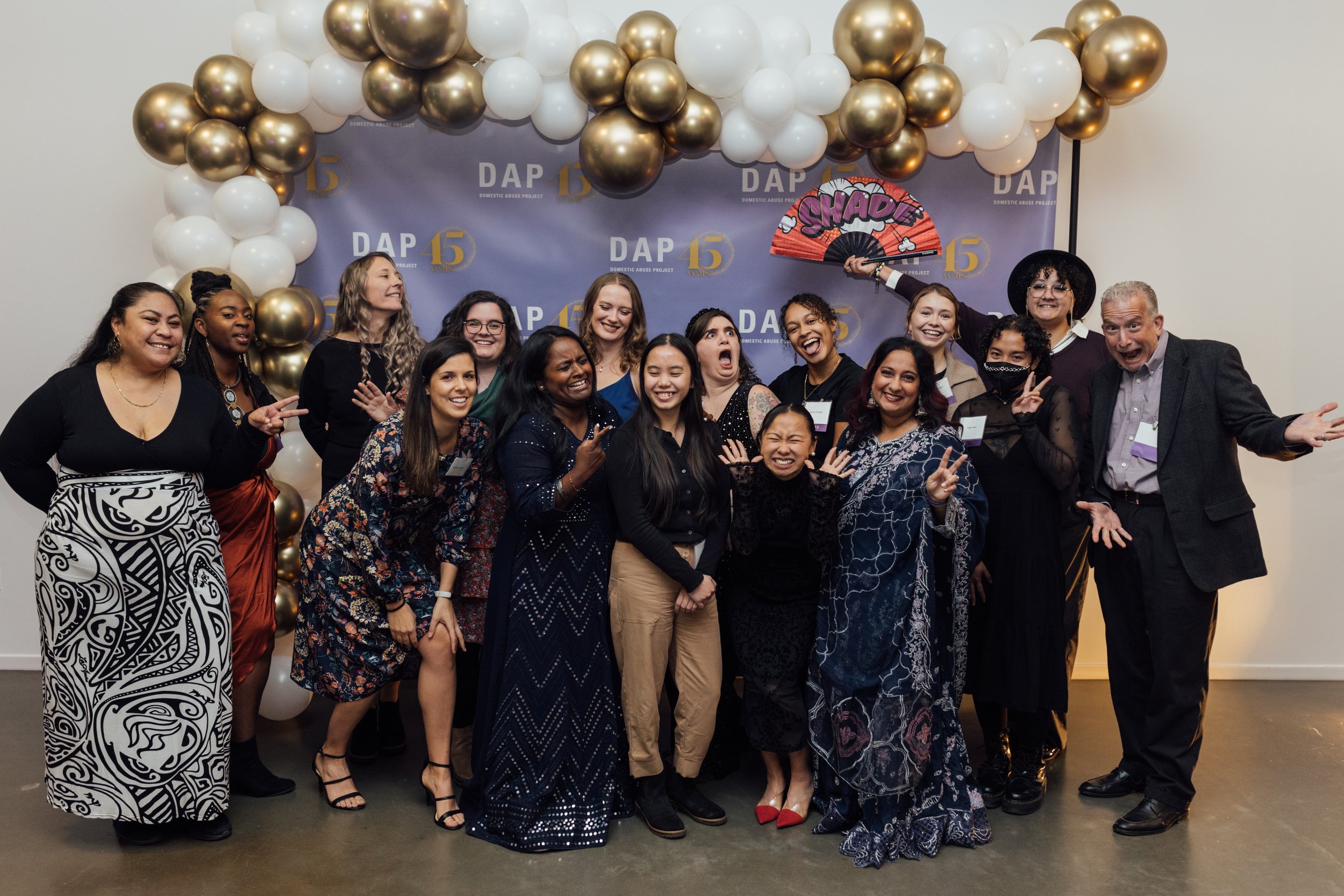 Group of people smiling and posing at a celebratory event with a backdrop featuring balloons and a sign reading 'DAP 45'.