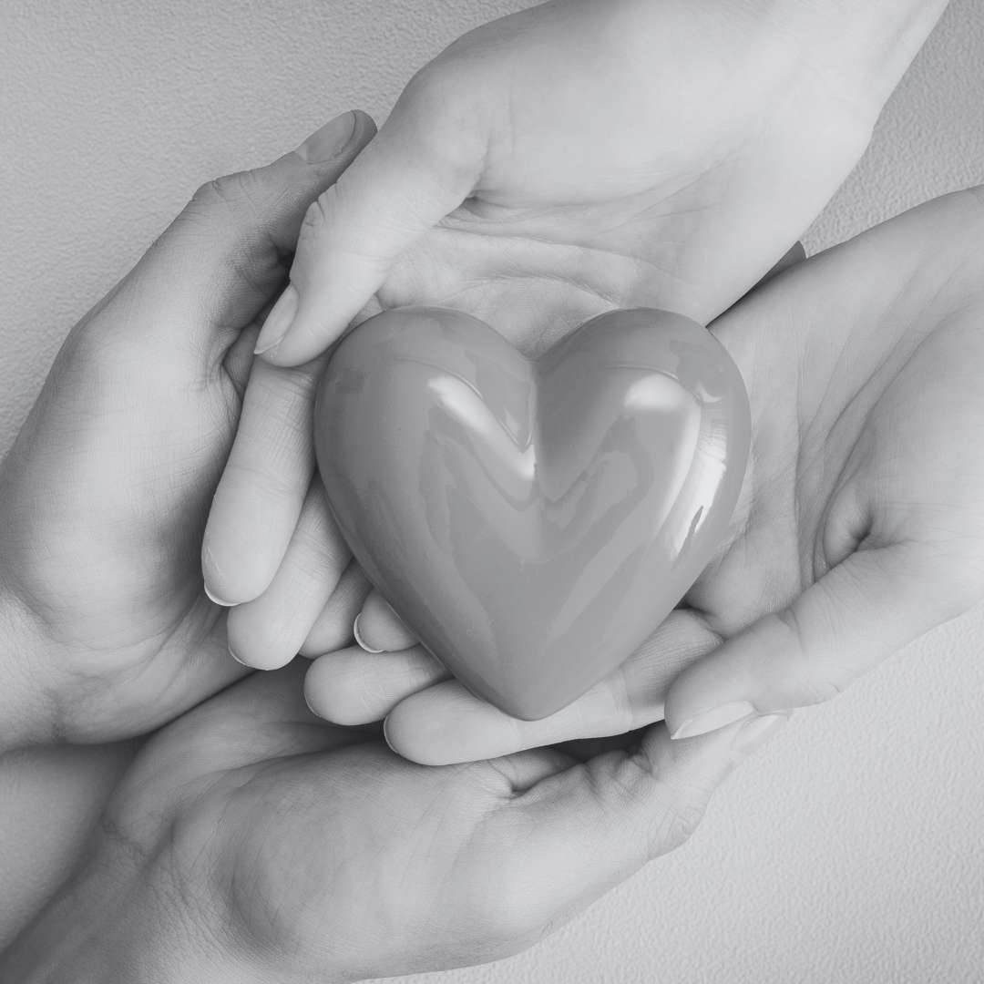 Two pairs of hands gently holding a glossy, heart-shaped object.