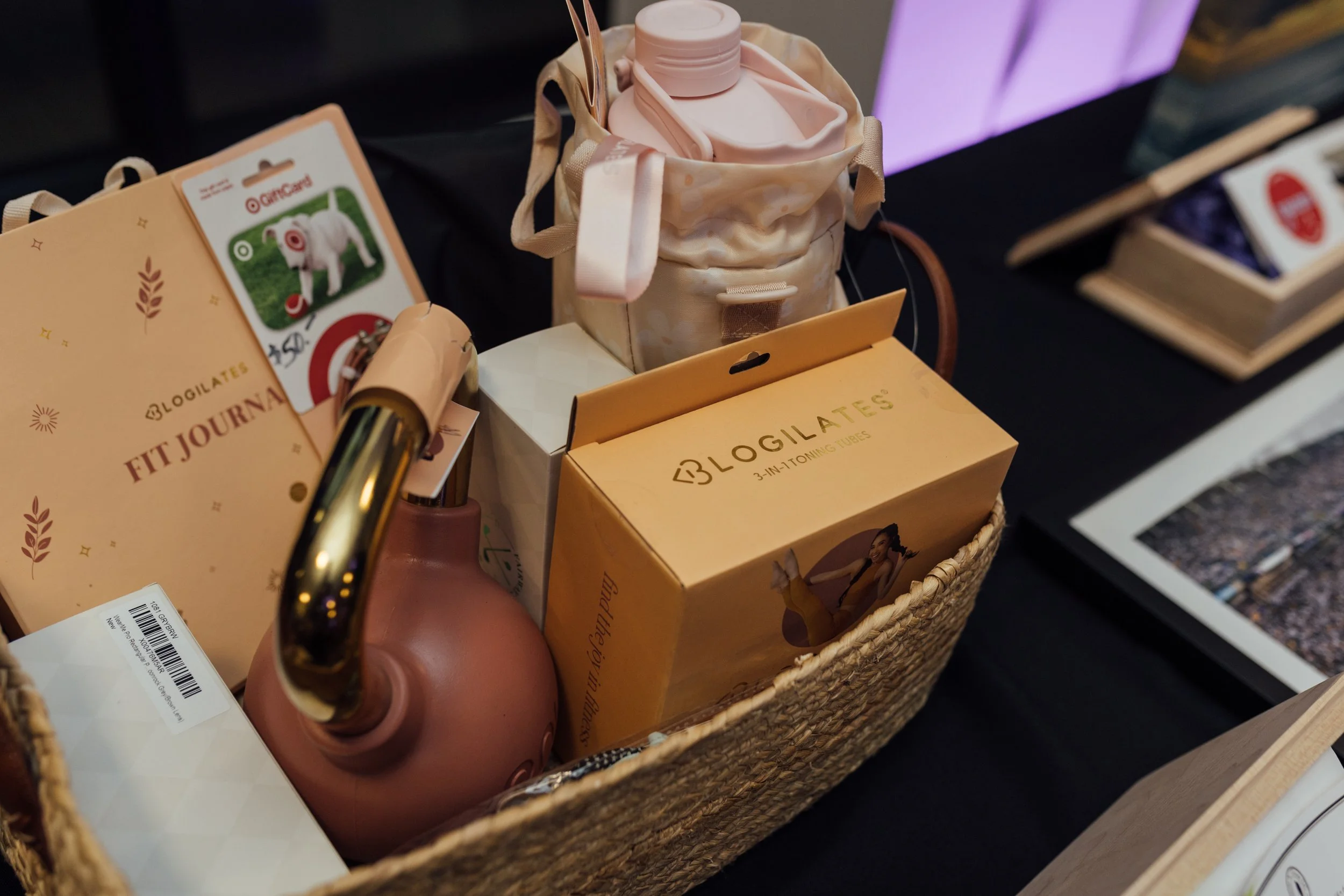 A woven basket containing a pink thermos, a yellow box labeled 'Blogilates', a fitness journal, and some small pamphlets at a display table.