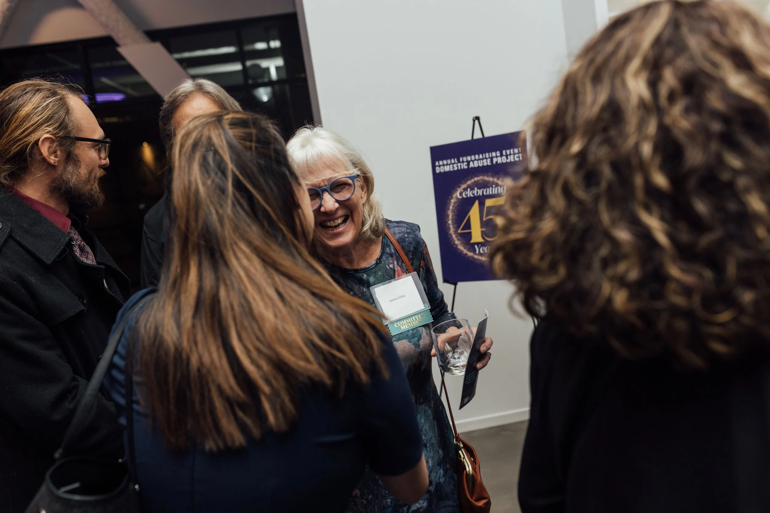 A group of people engaged in conversation at an event celebrating the 45th anniversary of the Domestic Abuse Project, with a woman smiling and wearing a name tag.