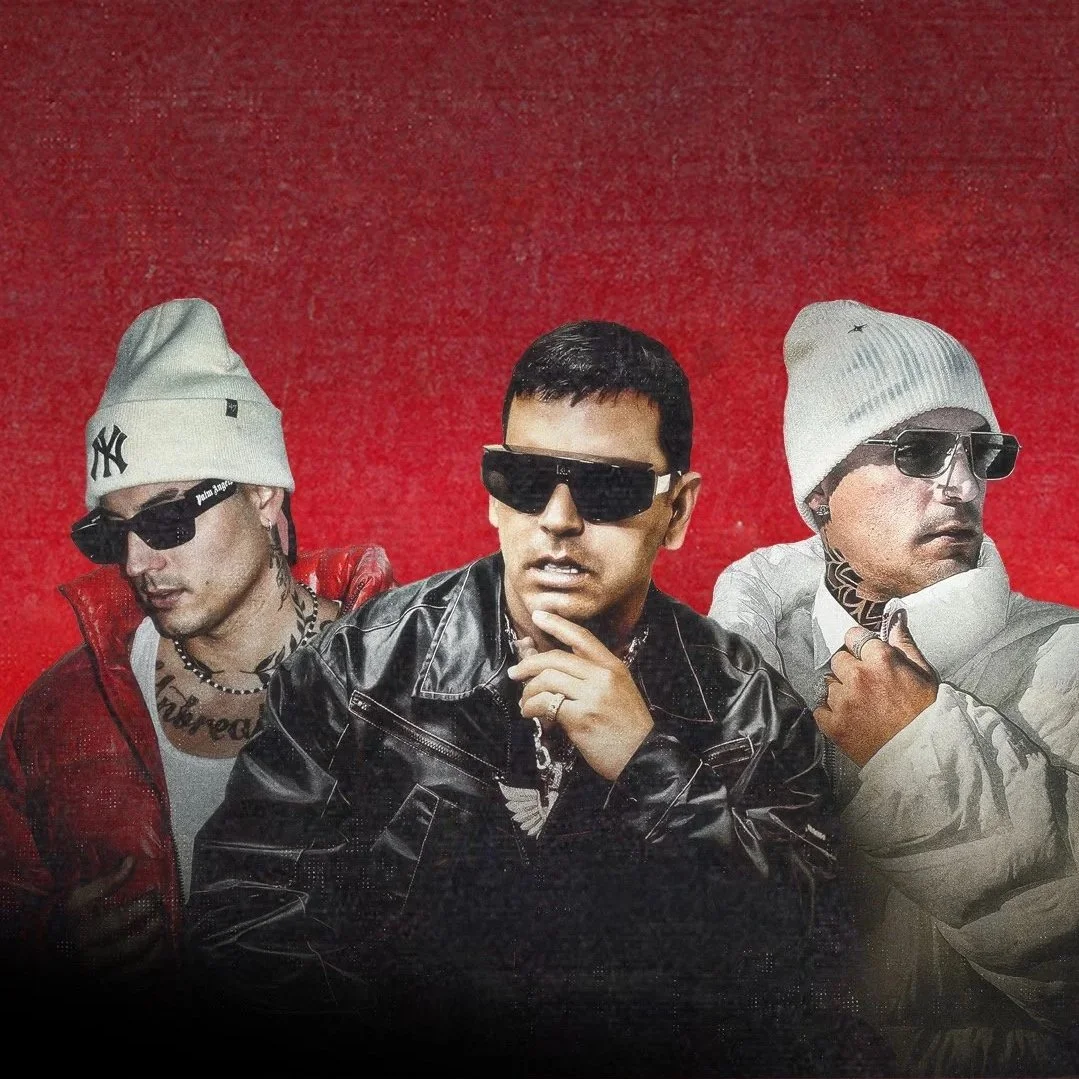 Tres hombres con gafas oscuras y ropa de moda posando frente a un fondo rojo. Tito el bambino, dale pututi y Nesty