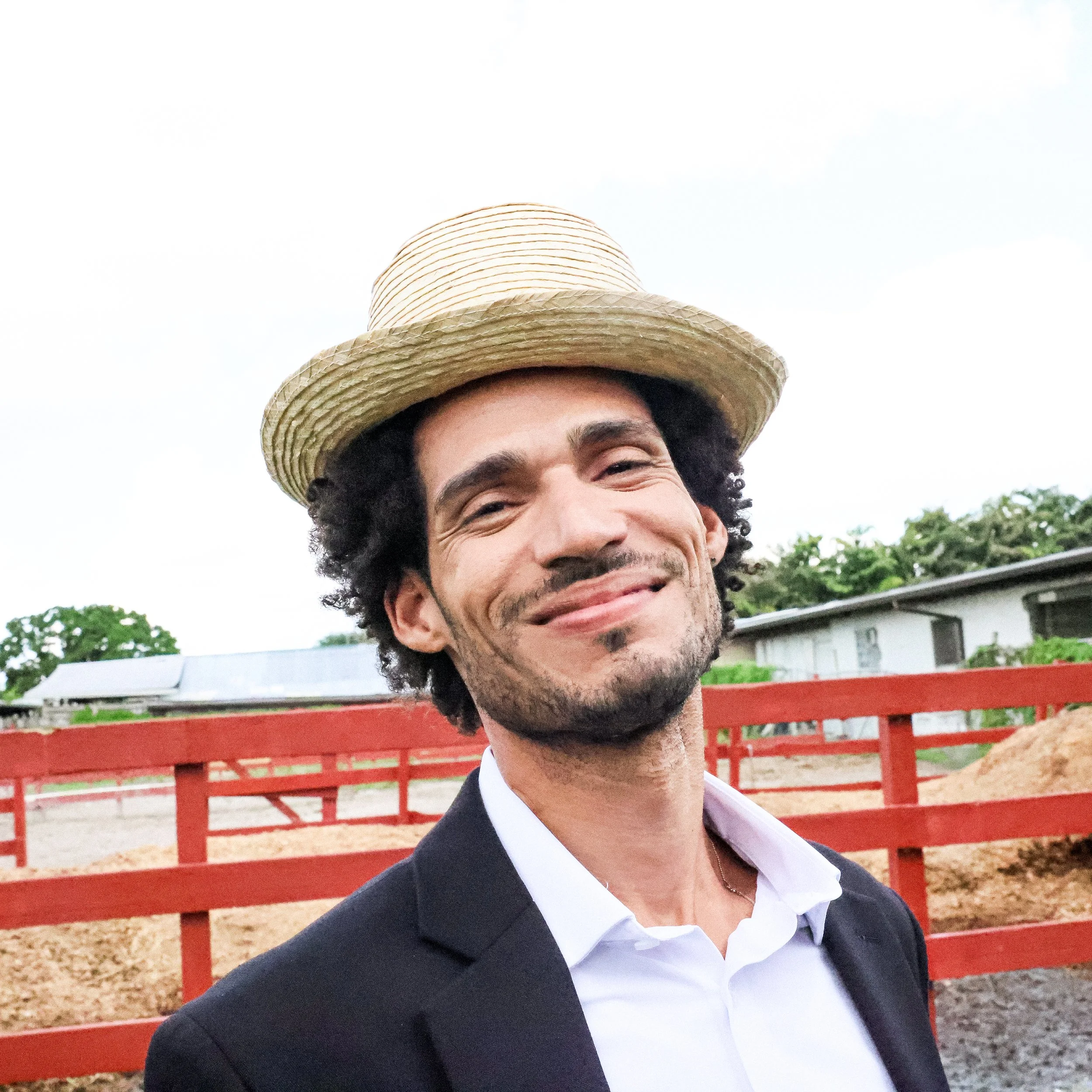 Ronkalunga. Hombre sonriendo con sombrero de paja, ropa formal, fondo de campo y establo.