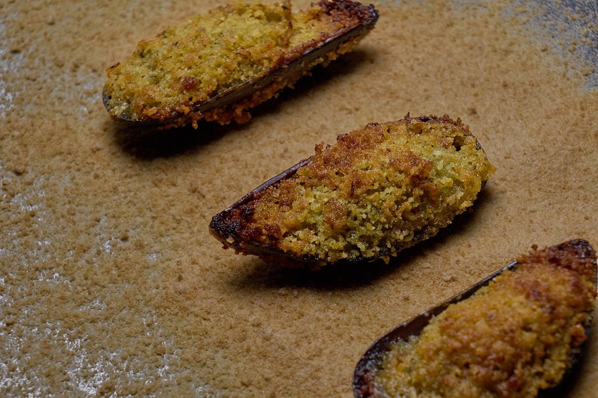 Three baked stuffed eggplant halves with breadcrumb topping on a baking sheet with a breading mixture.