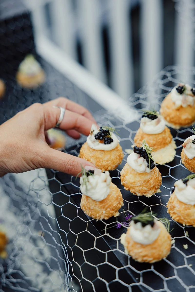A person is arranging small, round appetizers topped with cream and black caviar on a wire rack. The appetizers are golden-brown and look crispy.