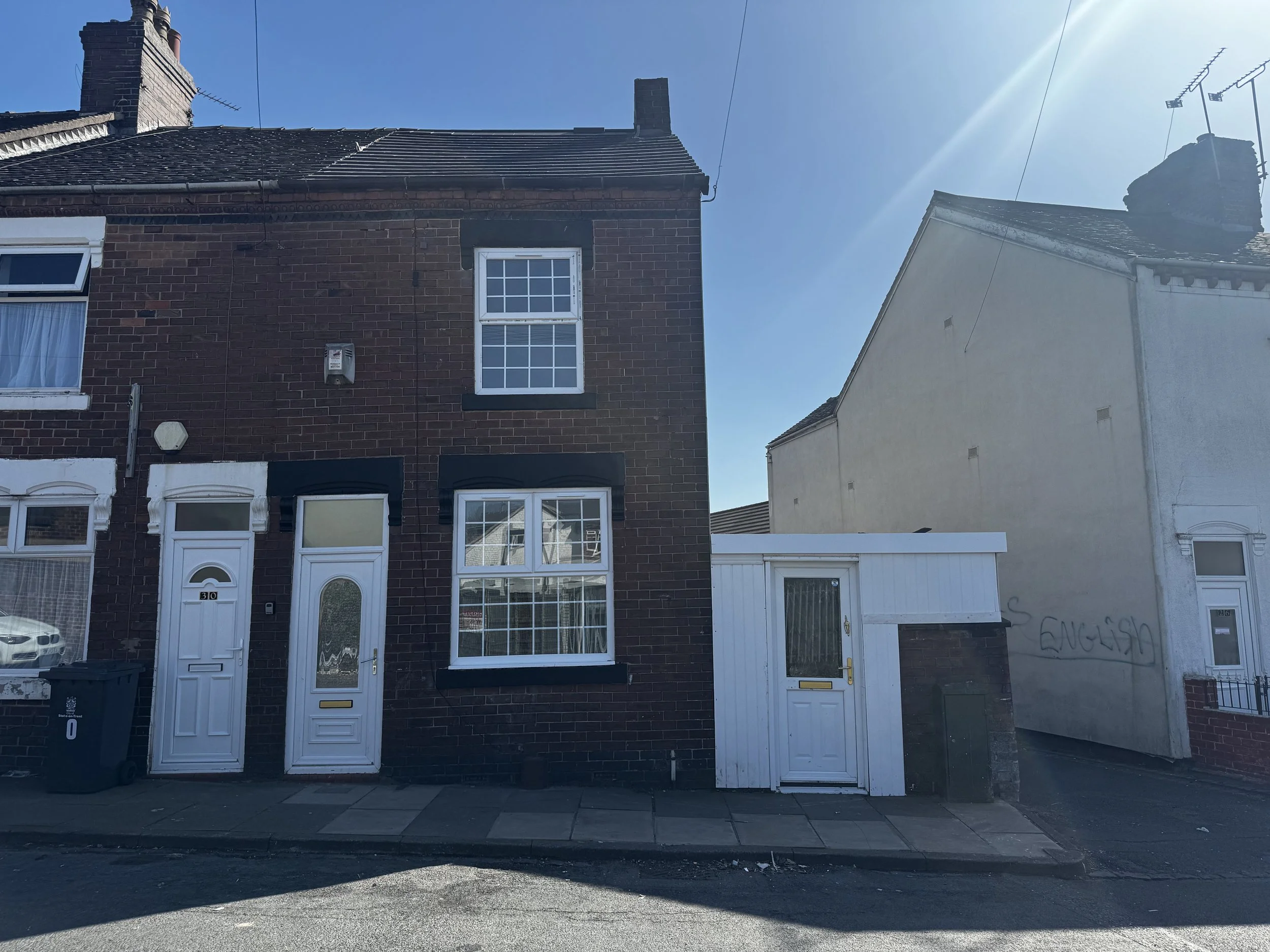 Front elevation of a two/three bedroom end terrace house on Hillary Street, Cobridge, featuring brick exterior, white uPVC windows and doors, and a side storage area.