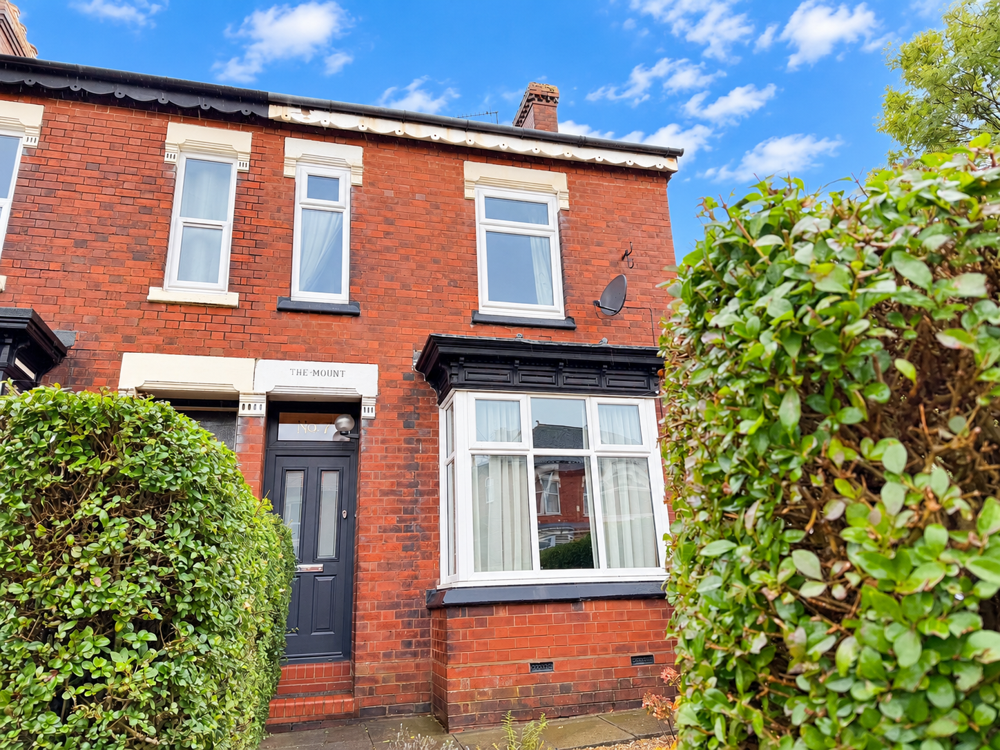 Victorian red brick end town house on Oakhill Avenue, Stoke-on-Trent, featuring a black front door, white-framed bay window, decorative period brickwork and mature front hedges.
