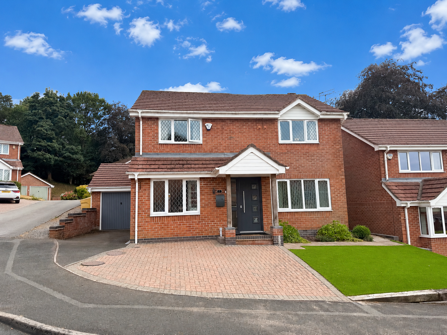Front elevation of a beautifully presented four-bedroom executive detached house on Hawksmoor Close, Lightwood, with block paved driveway, garage and landscaped front garden under a blue sky.