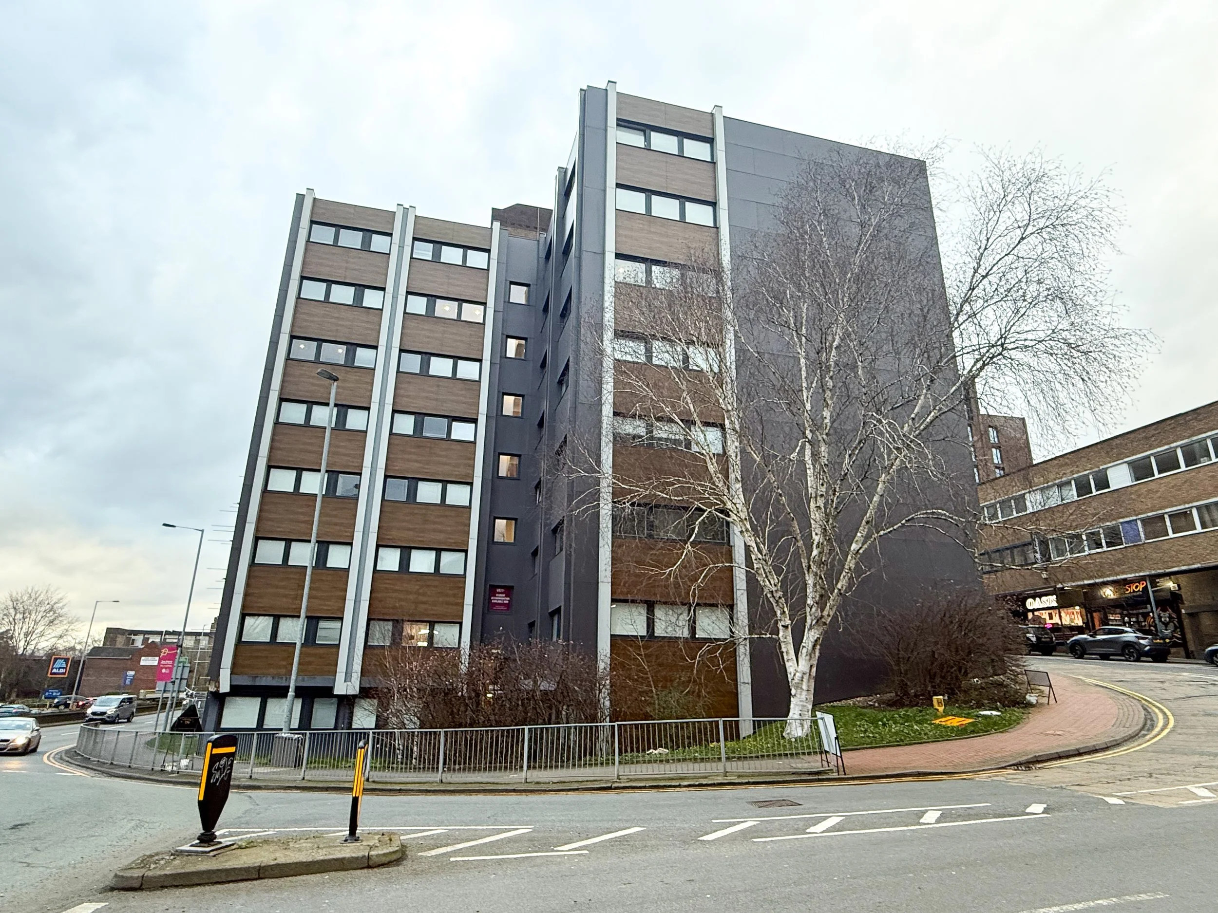 Exterior photograph of Keele House, a modern multi-storey student accommodation building on The Midway in Newcastle-under-Lyme, positioned on a corner plot near town centre amenities and main road links.