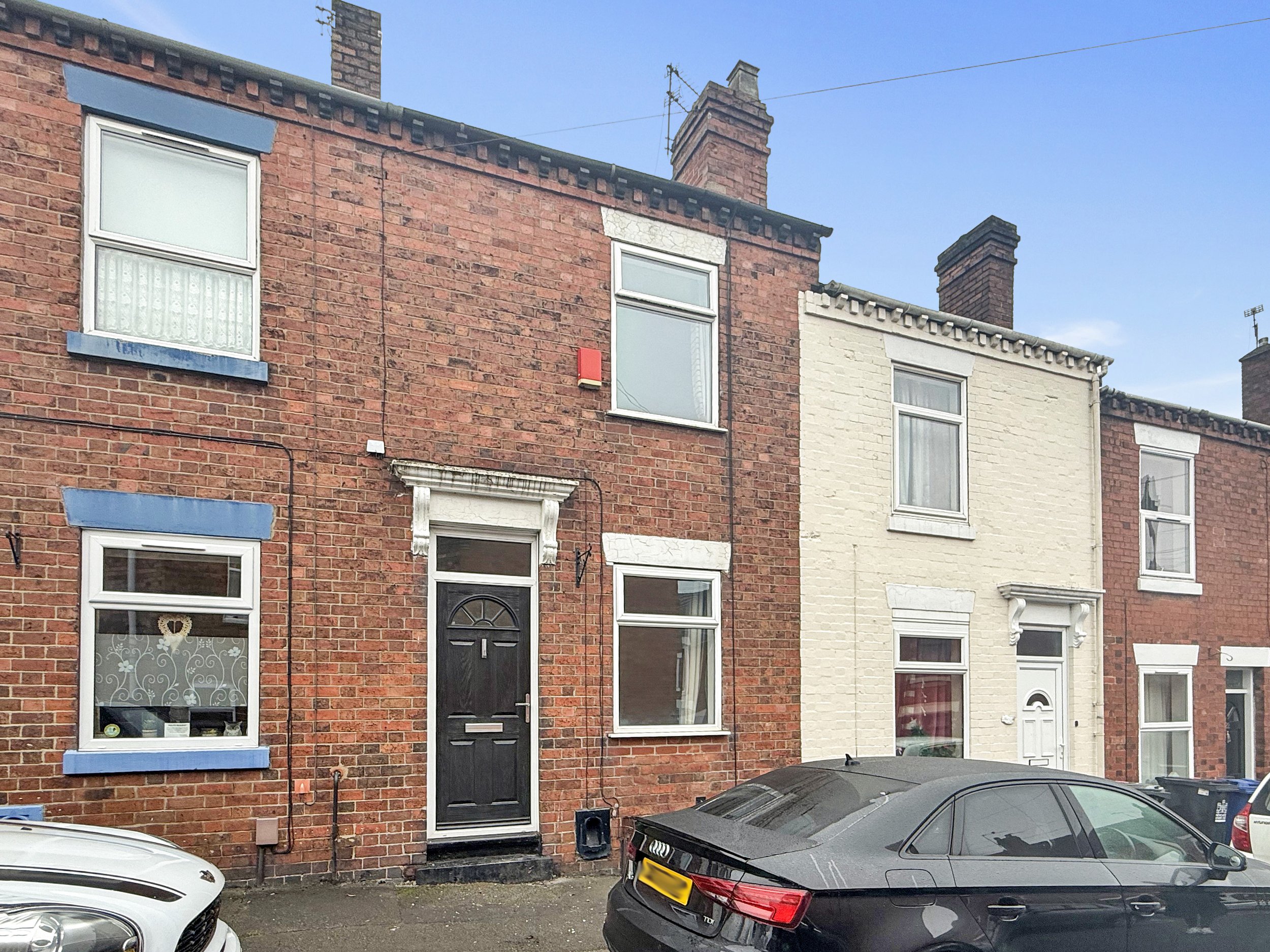 Front exterior of a traditional red brick two bedroom mid terraced house for sale on Duke Street, Newcastle-under-Lyme, Staffordshire, ST5 1NE, featuring a black front door and on-street parking.