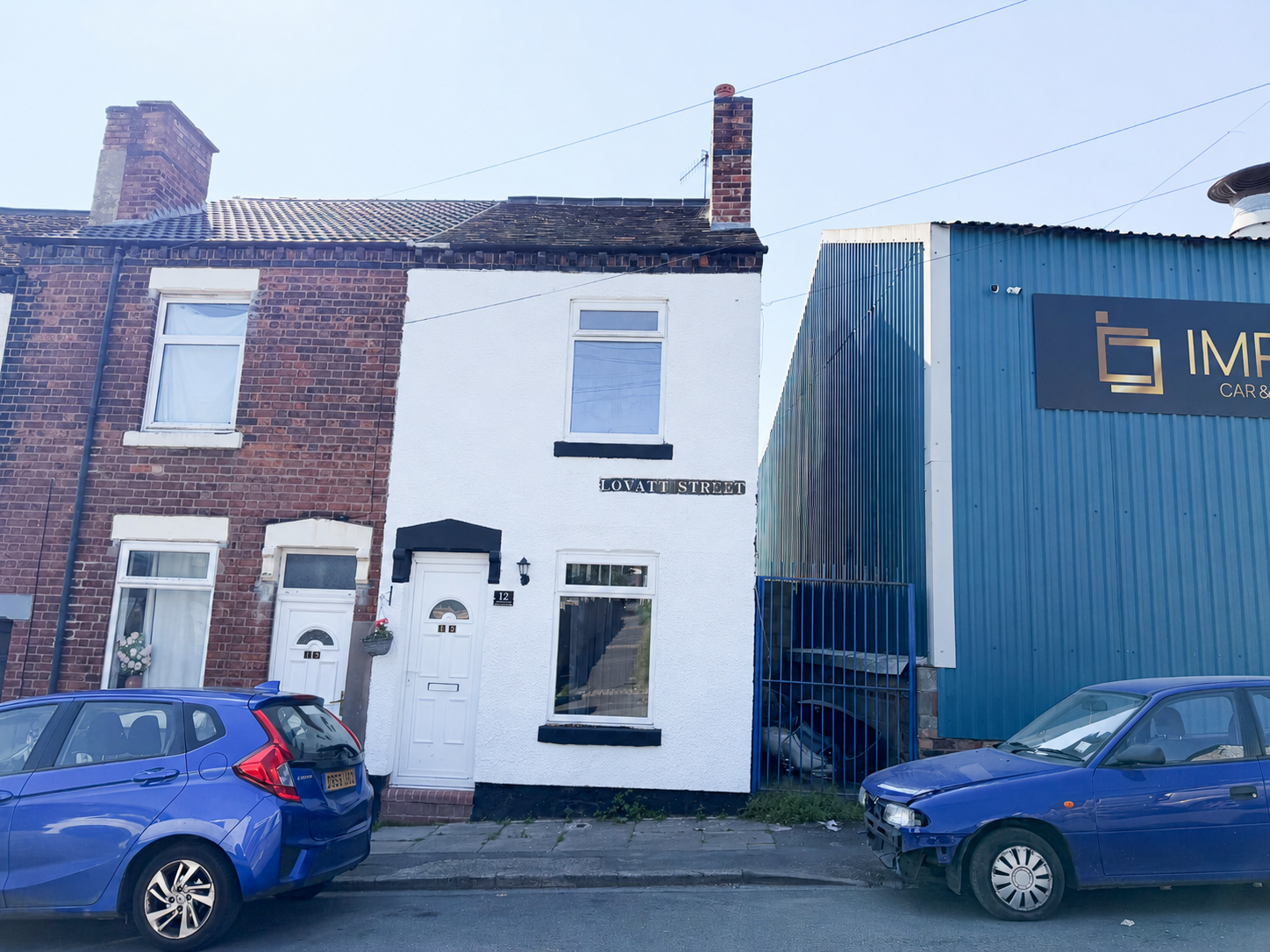 Front elevation of a refurbished white rendered two bedroom end terrace house on Lovatt Street, Stoke-on-Trent, with black trim, uPVC windows and door, under a clear blue sky.