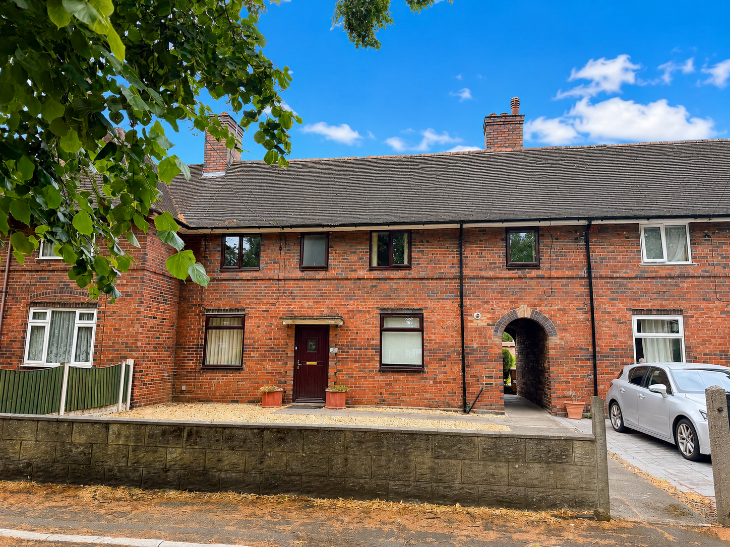 Front elevation of a spacious four-bedroom red brick town house on Harpfield Road, Trent Vale, with a low-maintenance front garden, attractive brick archway and mature trees overlooking the property.