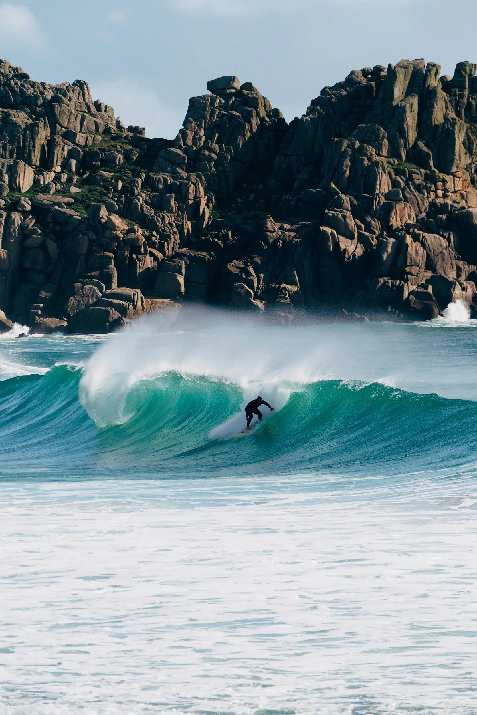 A surfer riding a wave near a rocky coastline.