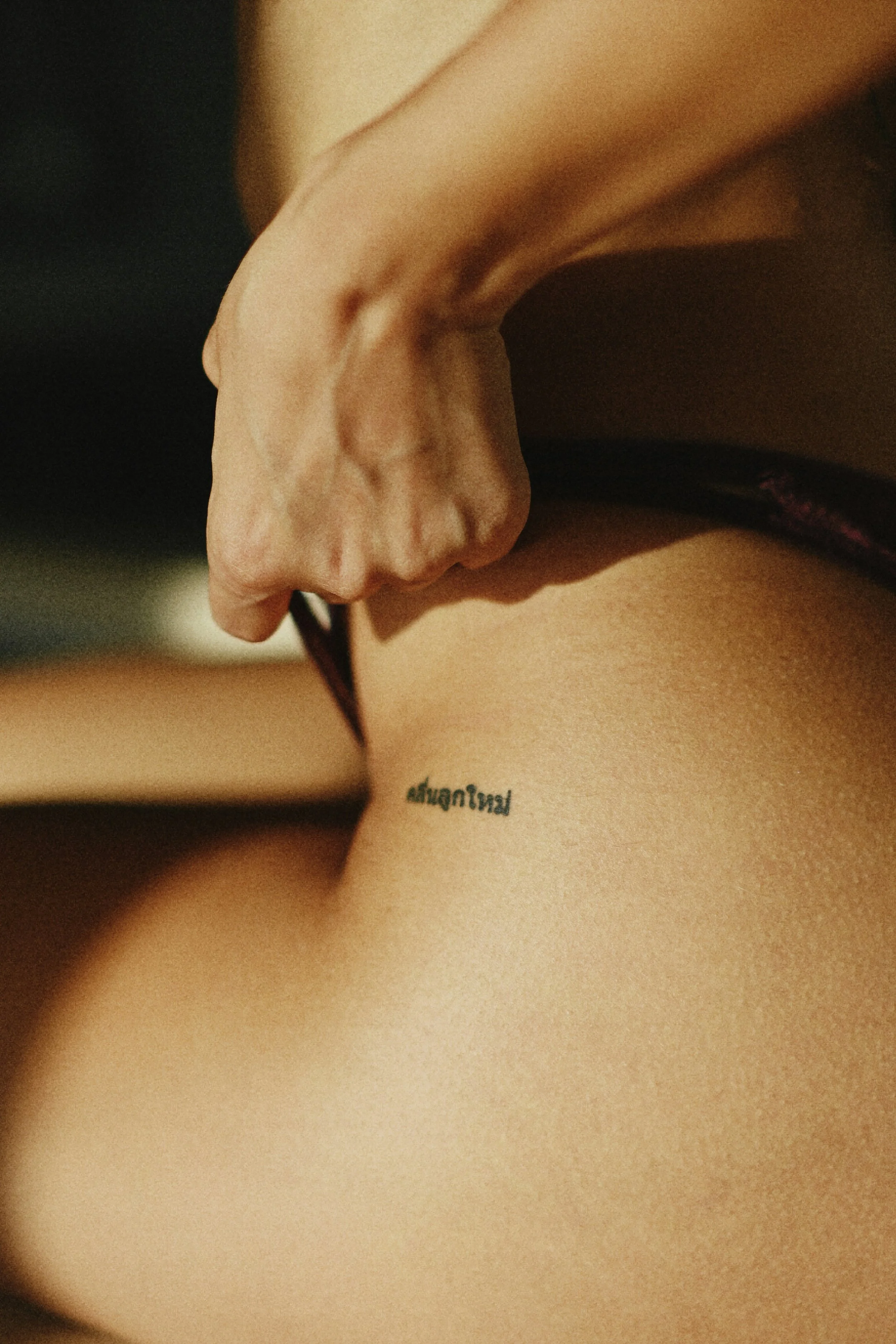 Close-up of a person's hand with their thumb and index finger pinching a small tattoo on their hip that has text in a foreign script.