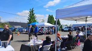 People gathered at an outdoor event with tents, tables, and chairs in a parking lot.