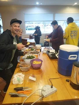 People preparing food and serving drinks in a casual indoor setting with a wooden table