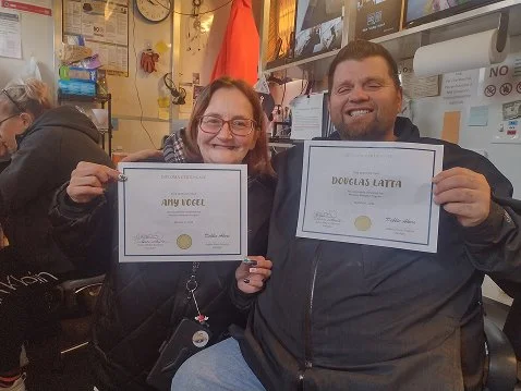 Two people holding certificates and smiling in an indoor setting.