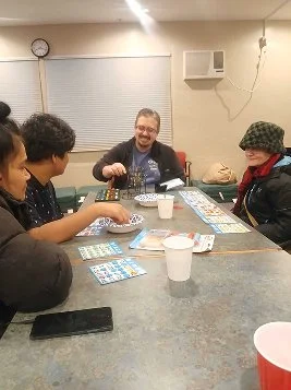 People playing a game at a table while an older man laughs.