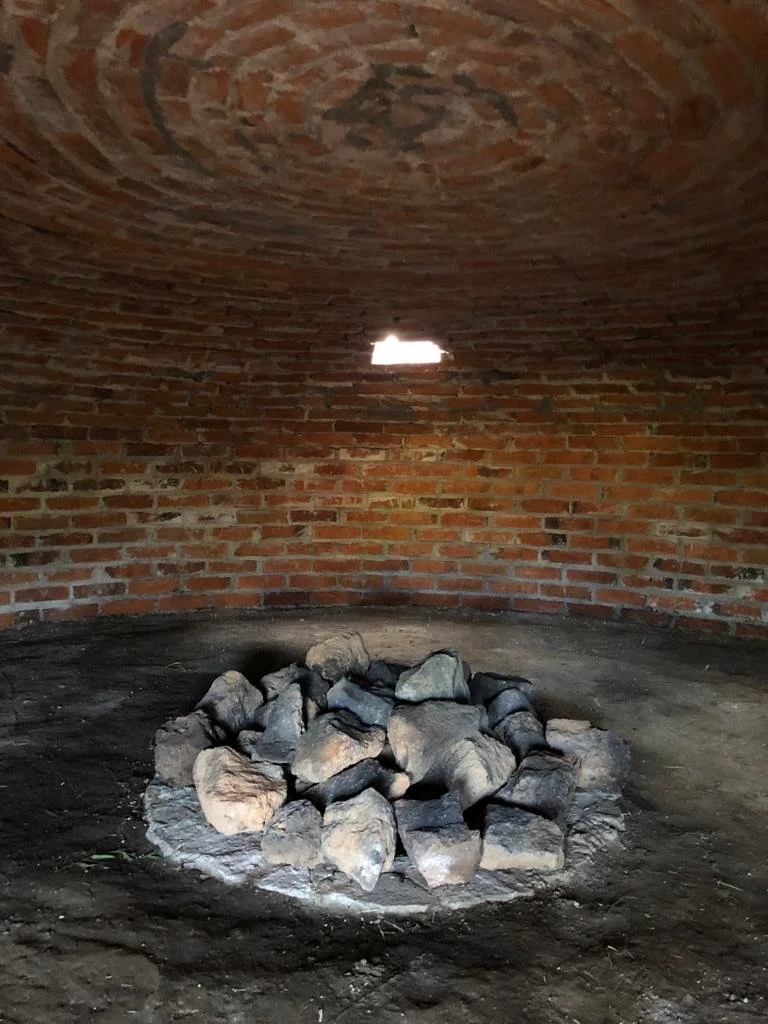 Interior de una estructura de ladrillos con un montón de piedras apiladas en el centro, luz que entra por una pequeña abertura en la pared.