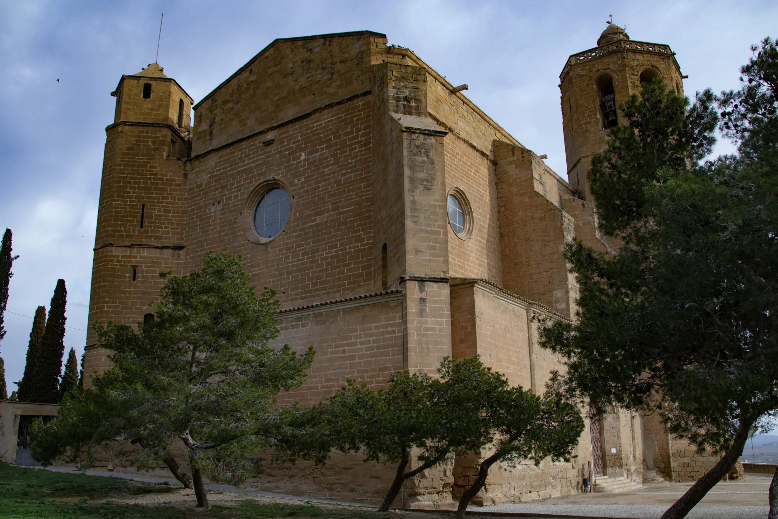 Vista exterior de Santa Maria de Balaguer amb el campanar i l’entorn arbrat.