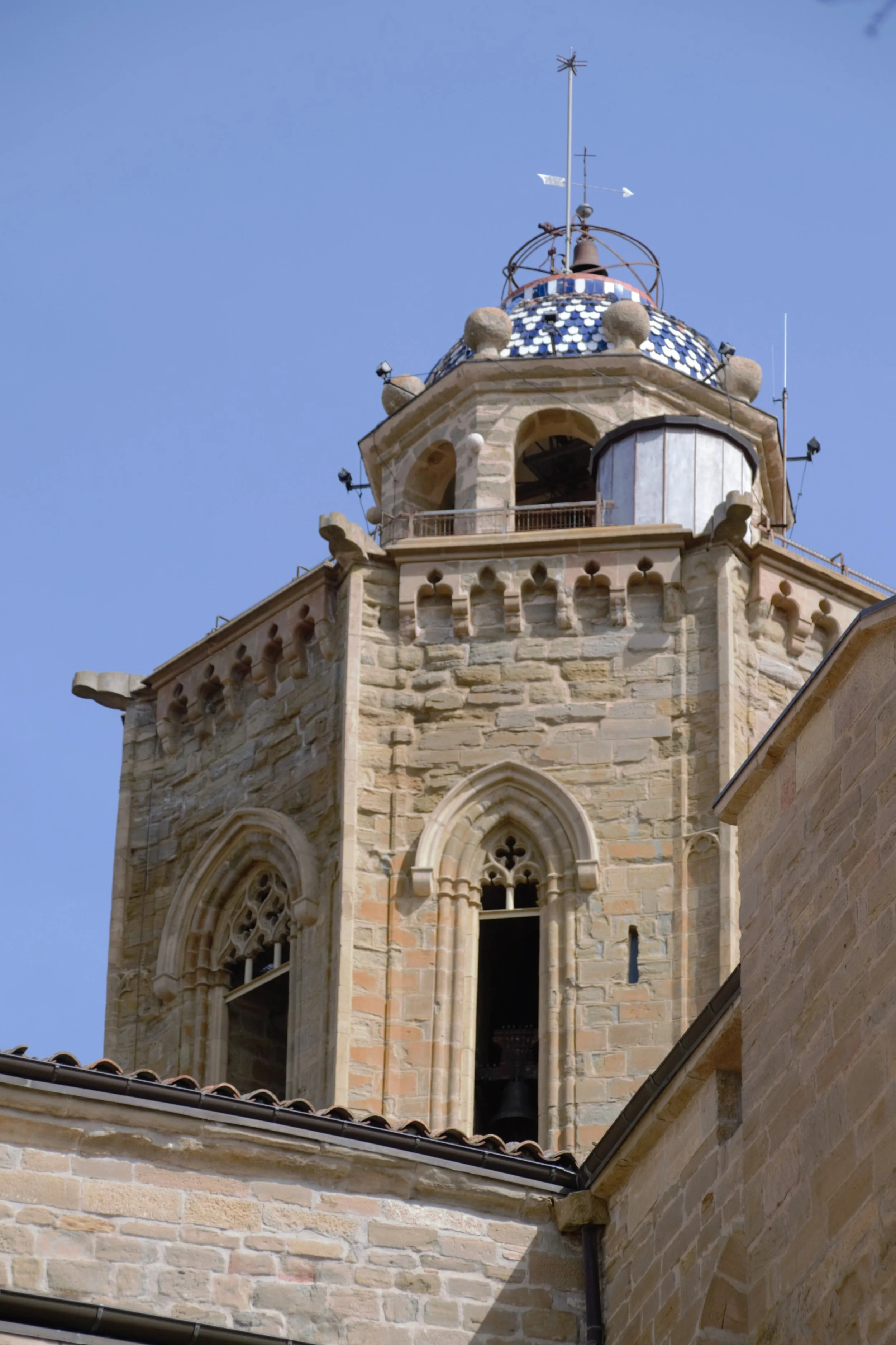 Detall superior del campanar de Santa Maria de Cervera amb finestrals gòtics i coberta decorada.