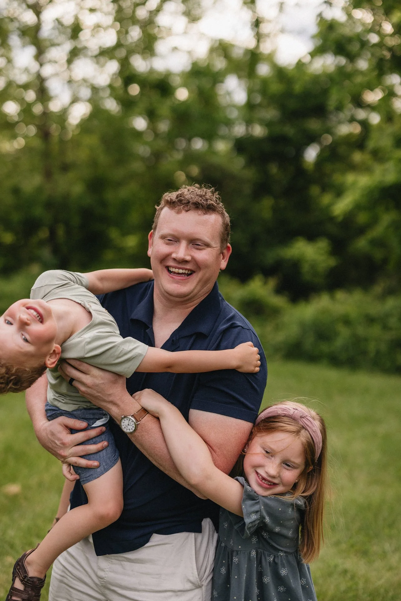 A laughing dad holding his son and hugging his daughter. They are all smiling and having fun during family photos in cincinnati.