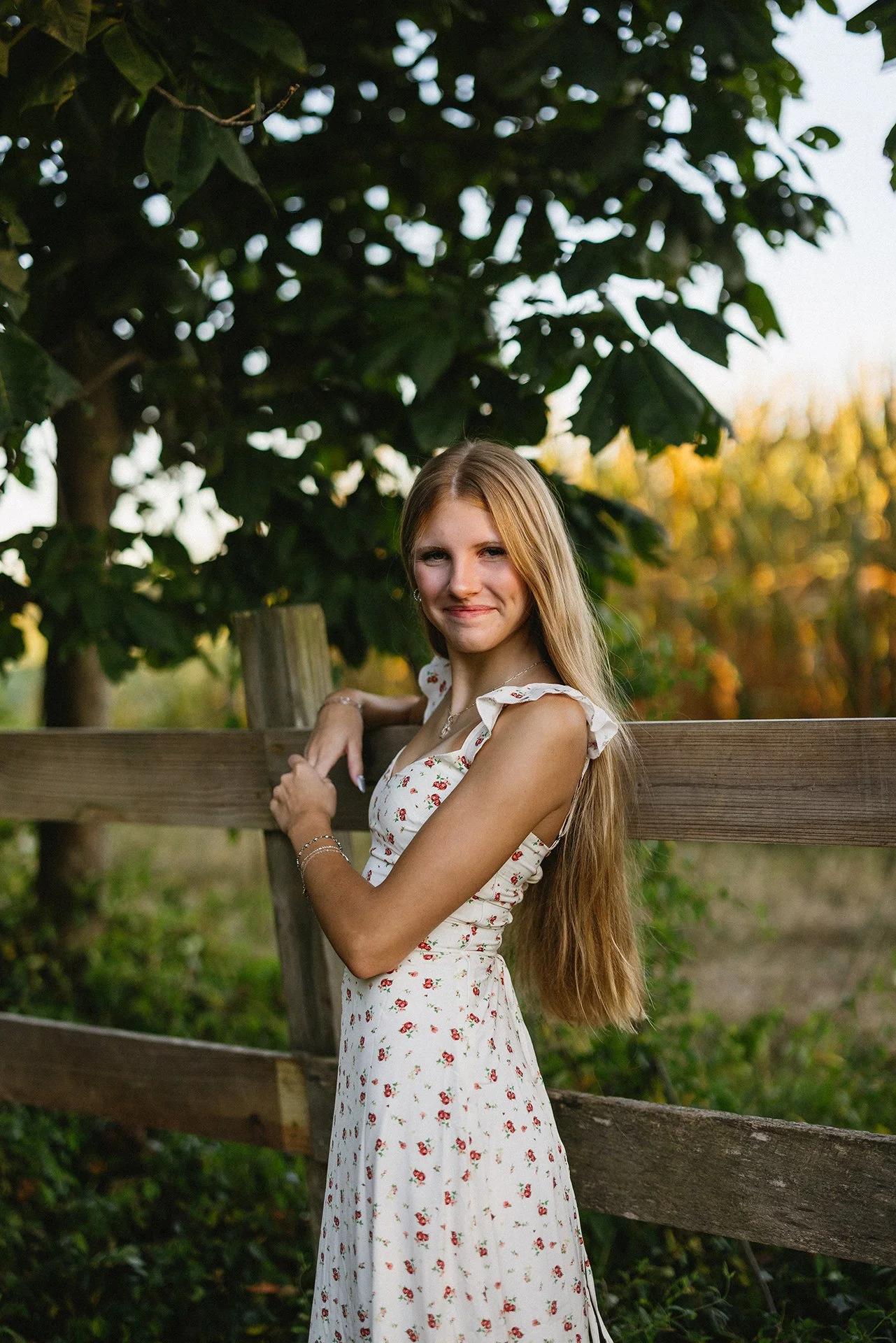 Lifestyle senior portrait in cincinnati ohio. A teen girl smiling by a fence outside during summer golden hour.