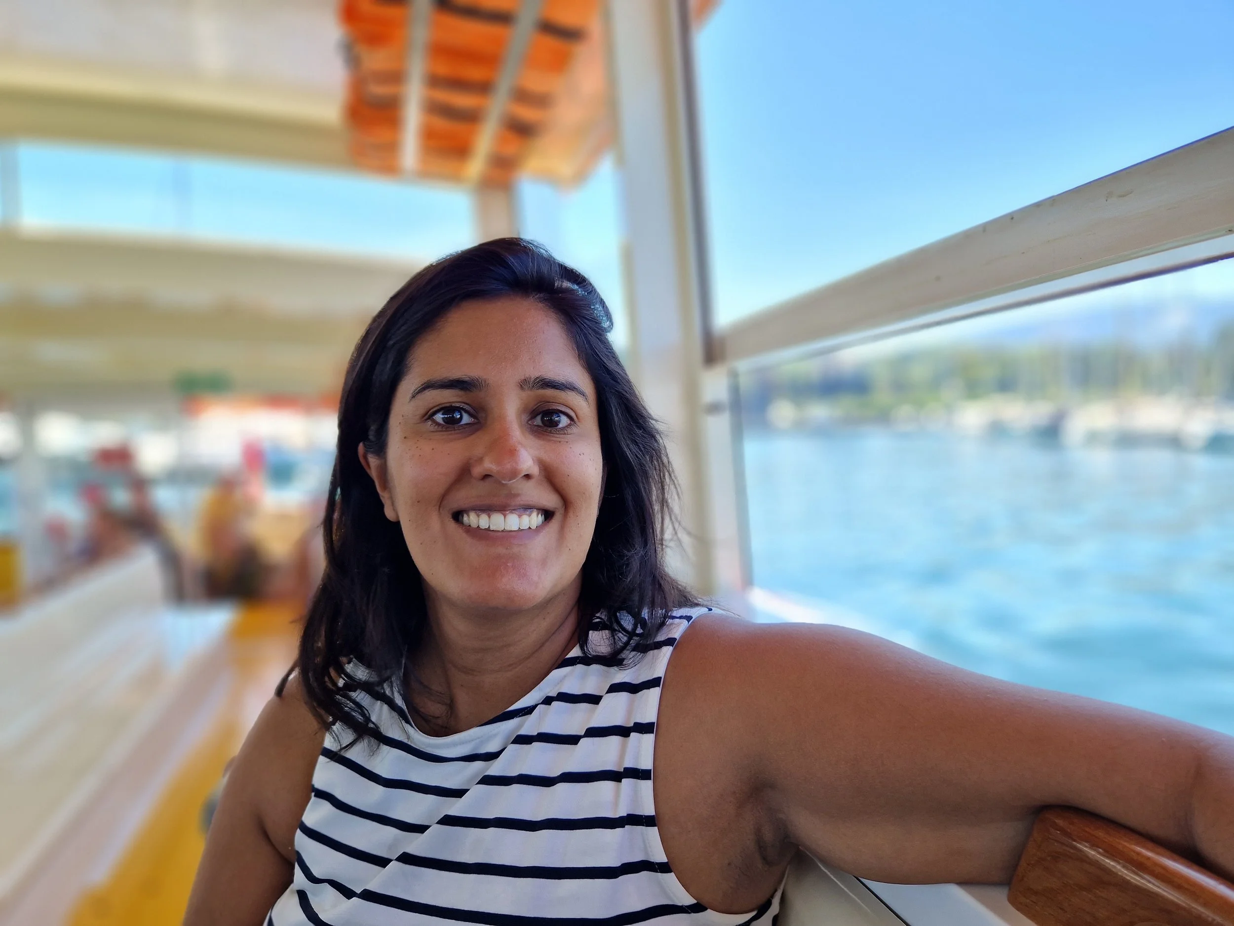 Preeti Dhillon wearing a sleeveless black and white striped dress and smiling, on a boat with water in the background.