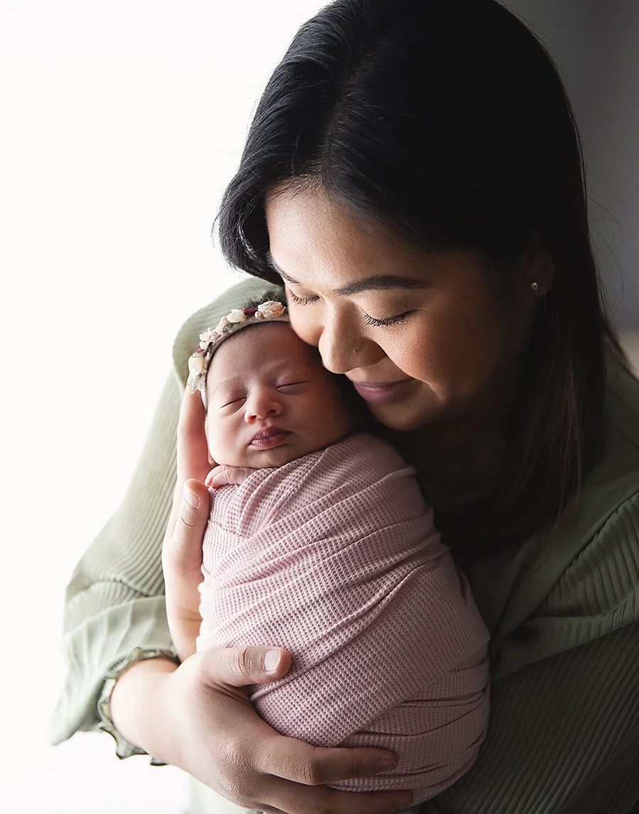 newborn baby snuggled in mom's arms surrounded by warm natural window light in greencastle pa newborn photography studio