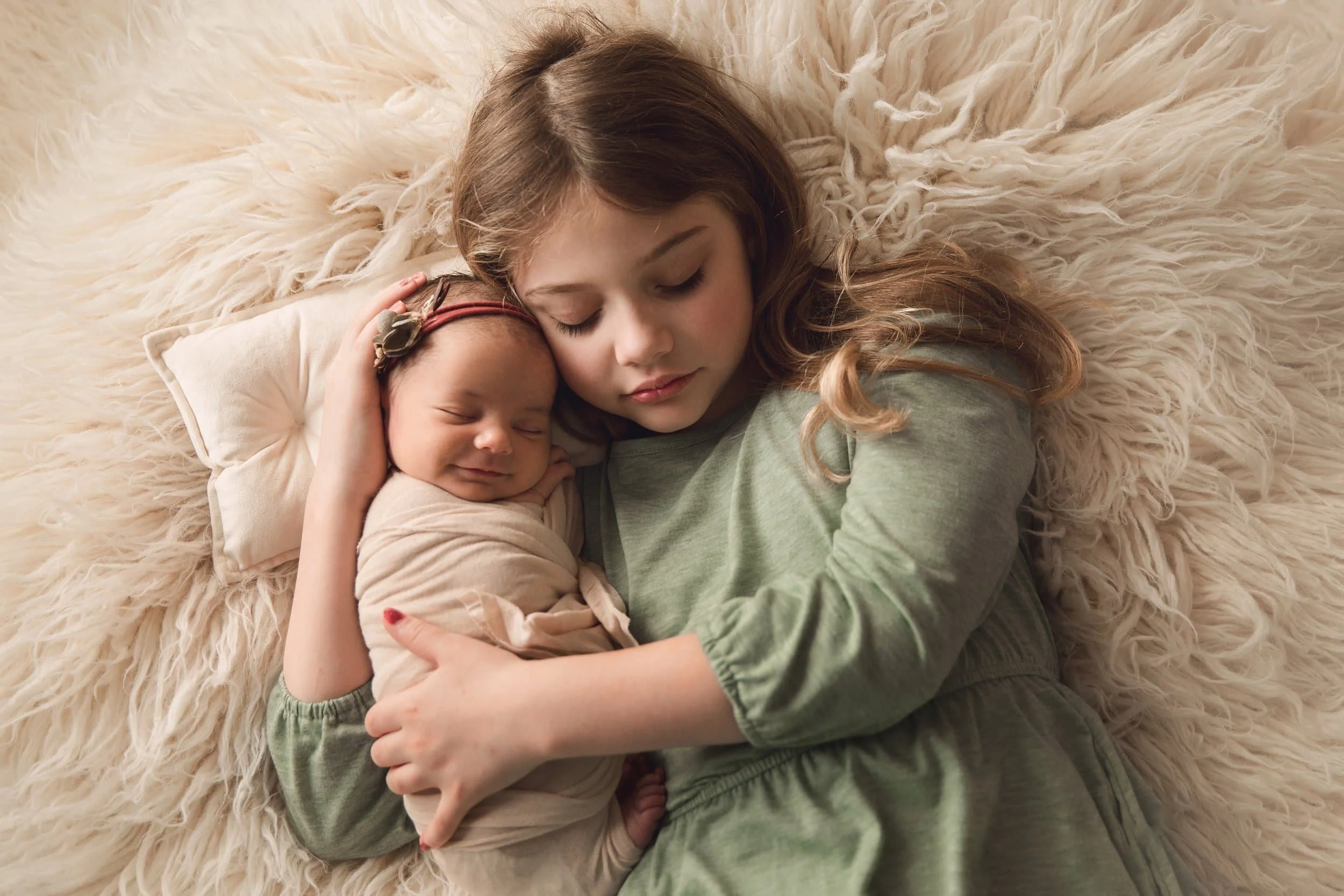 newborn and sibling in sage dress on neutral backdrop laying on back 