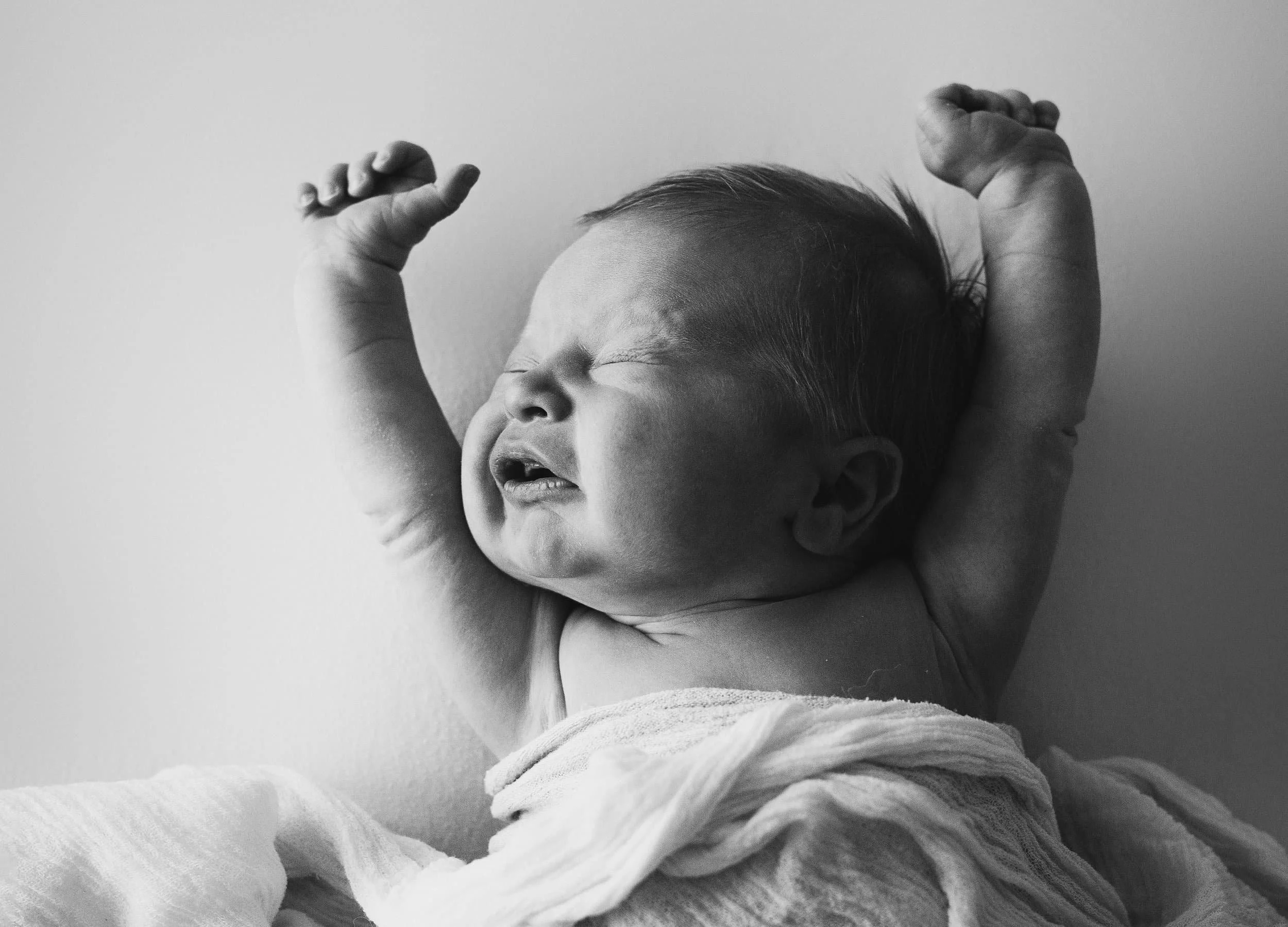 black and white image of newborn baby stretching on white backdrop
