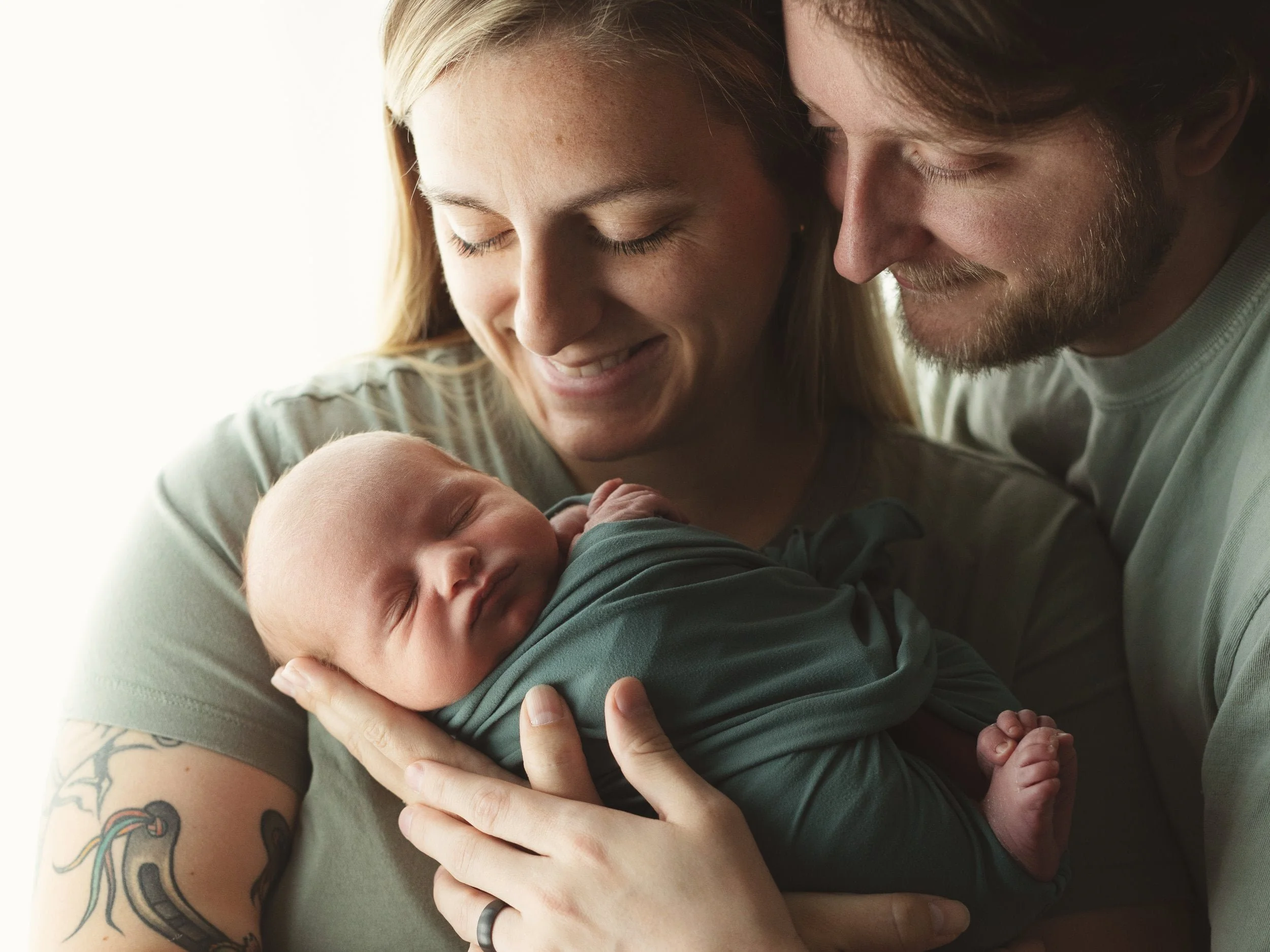 parents lovingly holding newborn baby in beautiful window light