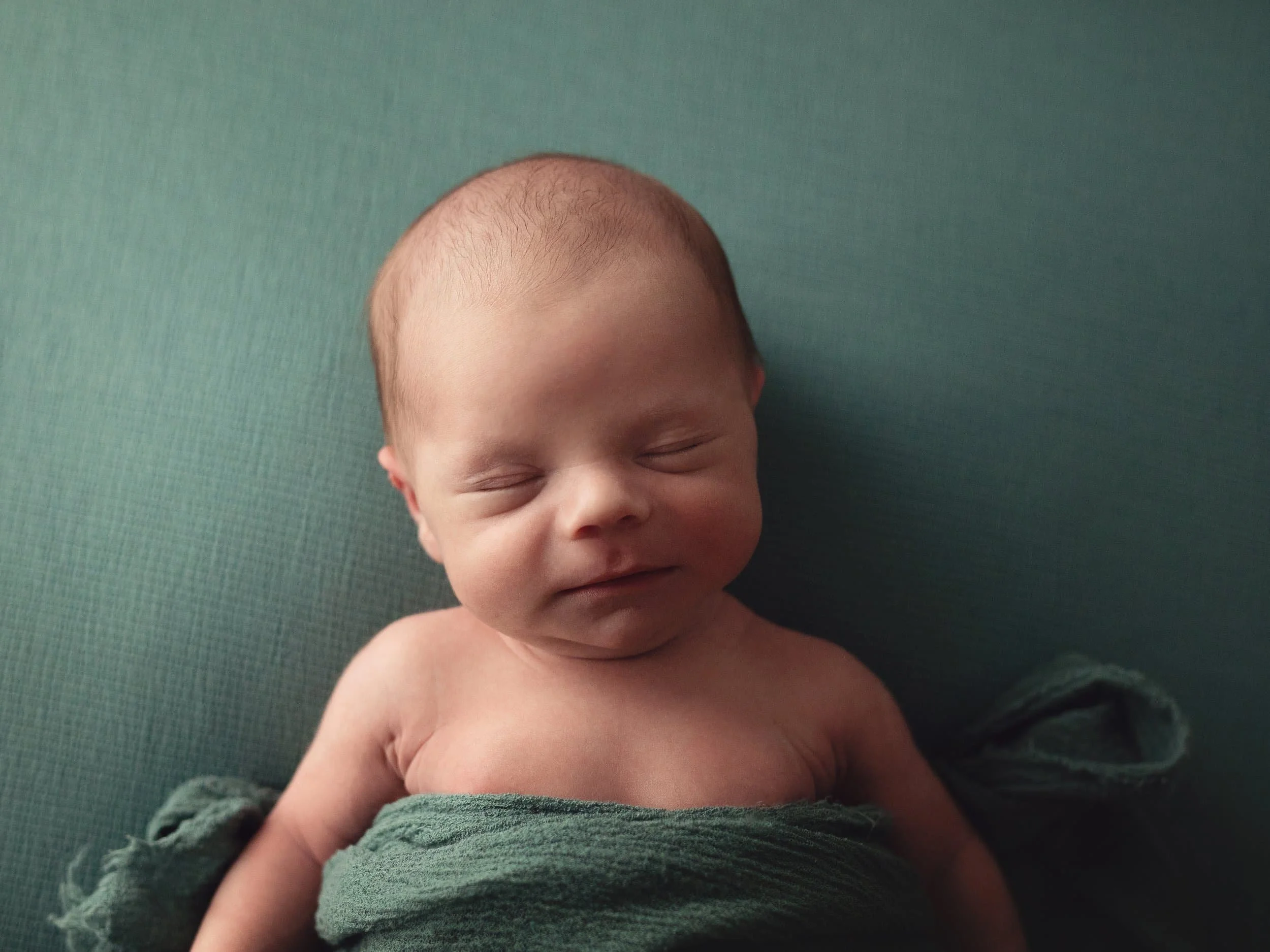 newborn with cute smirk laying on back on teal fabric