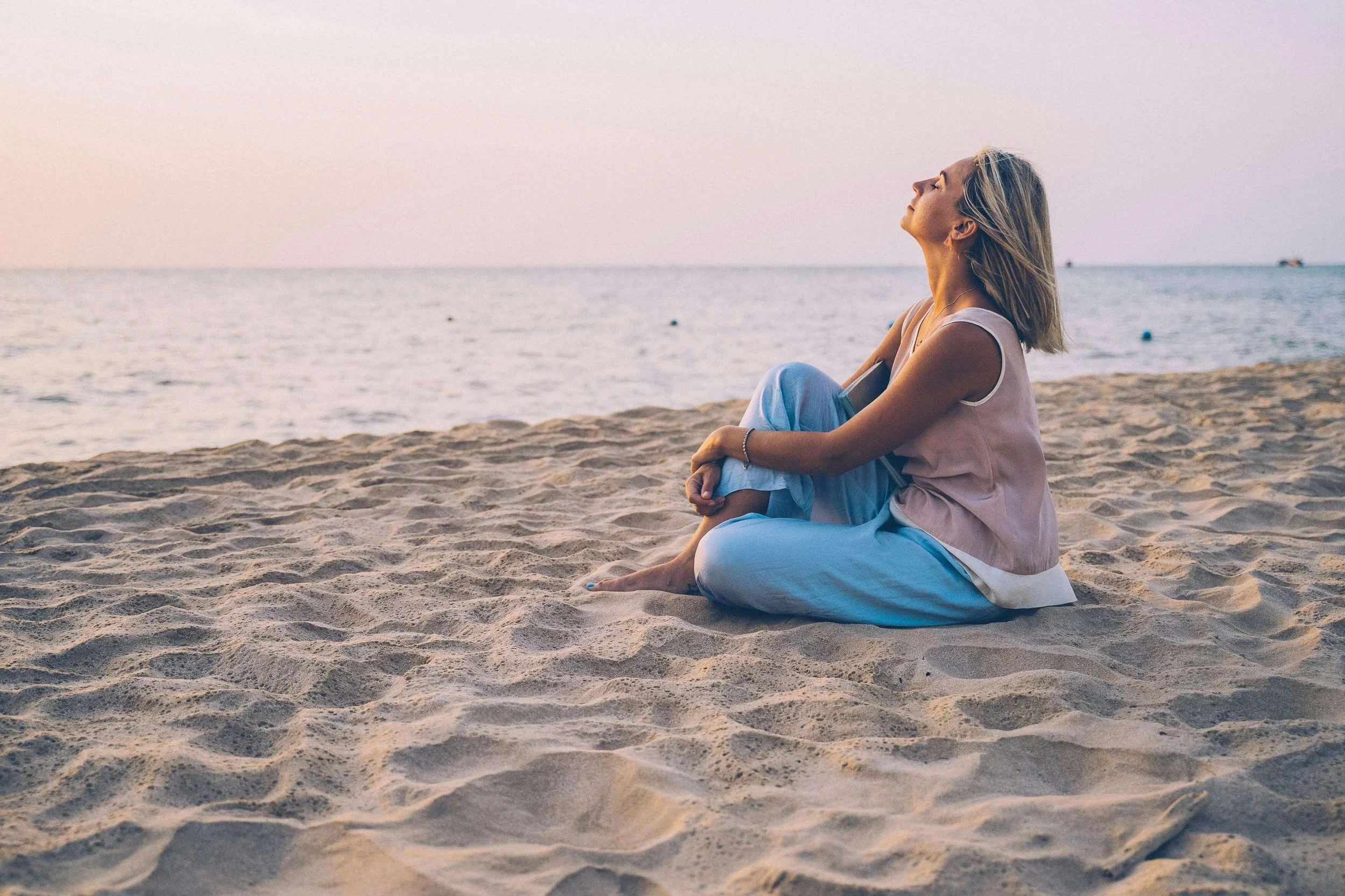Woman sitting on beach sand looking up at sky during sunset. Find relief from trauma, anxiety, and painful memories with EMDR therapy in Tampa, FL.