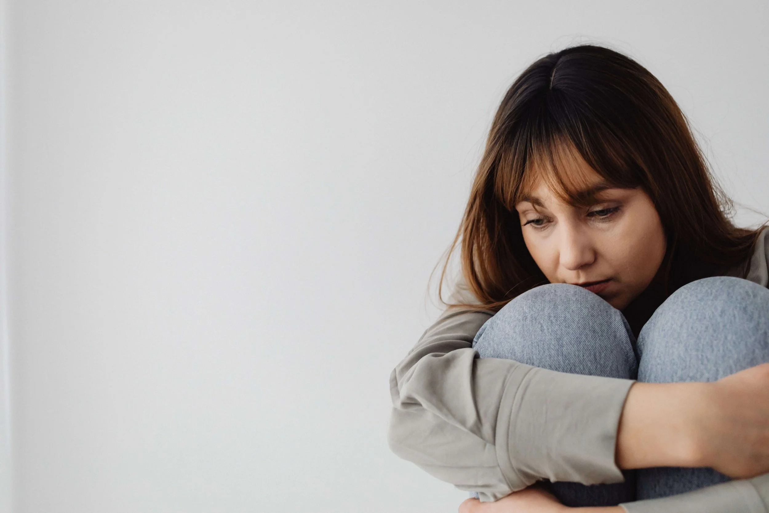 A woman with brown hair sitting on the floor hugging her knees to her chest. You do not have to keep sitting with the weight of it alone because anxiety therapy in Tampa, FL gives you a real path toward feeling like yourself again.